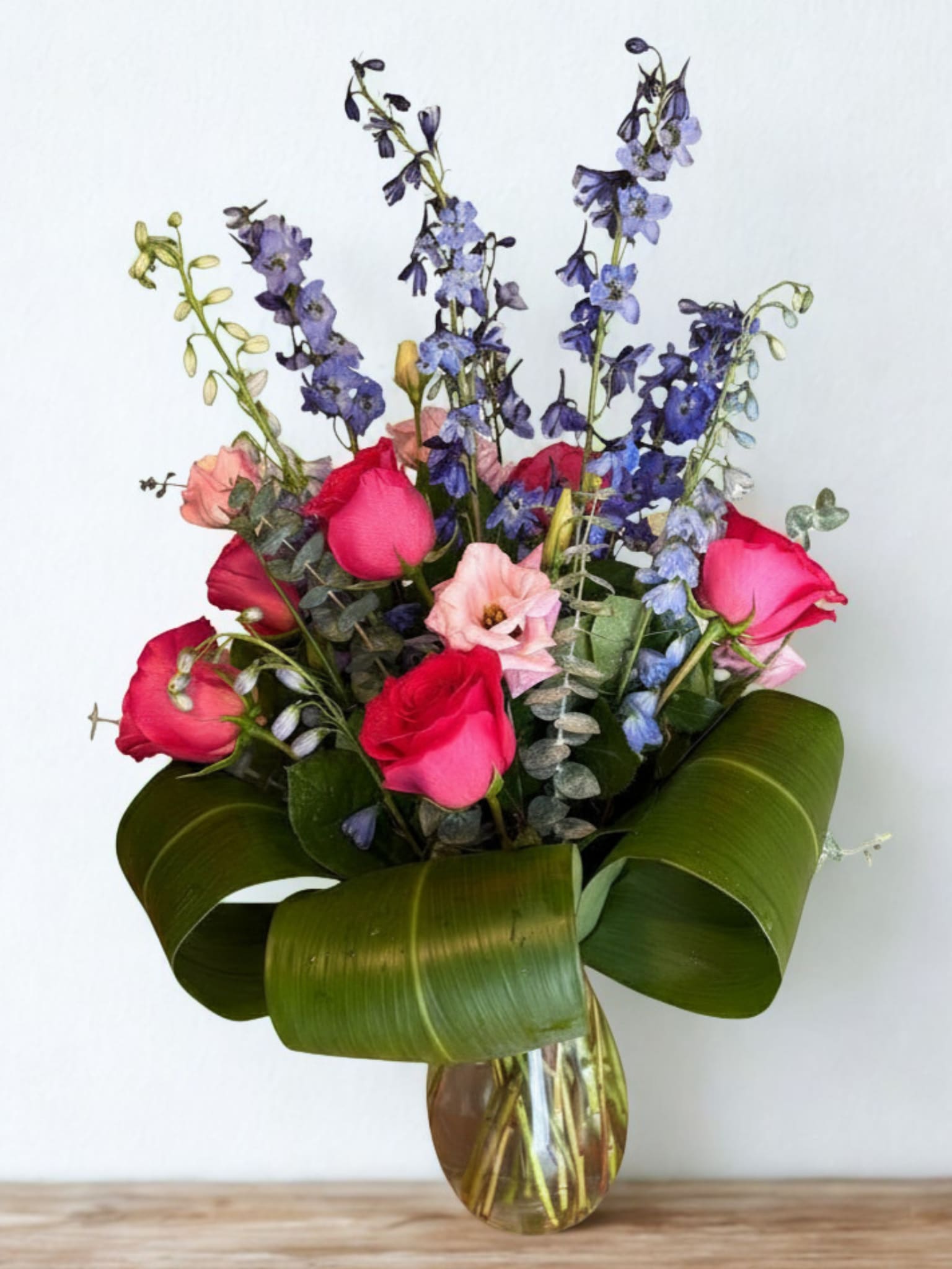 Blue and pink hapiness - Featuring  leaves, delphinium, roses, and eucalyptus, this blue, green, and pink arrangement make a big impact. Blue Lagoon is cool enough for any summer day.  Approximate Dimensions: 25"D x 32