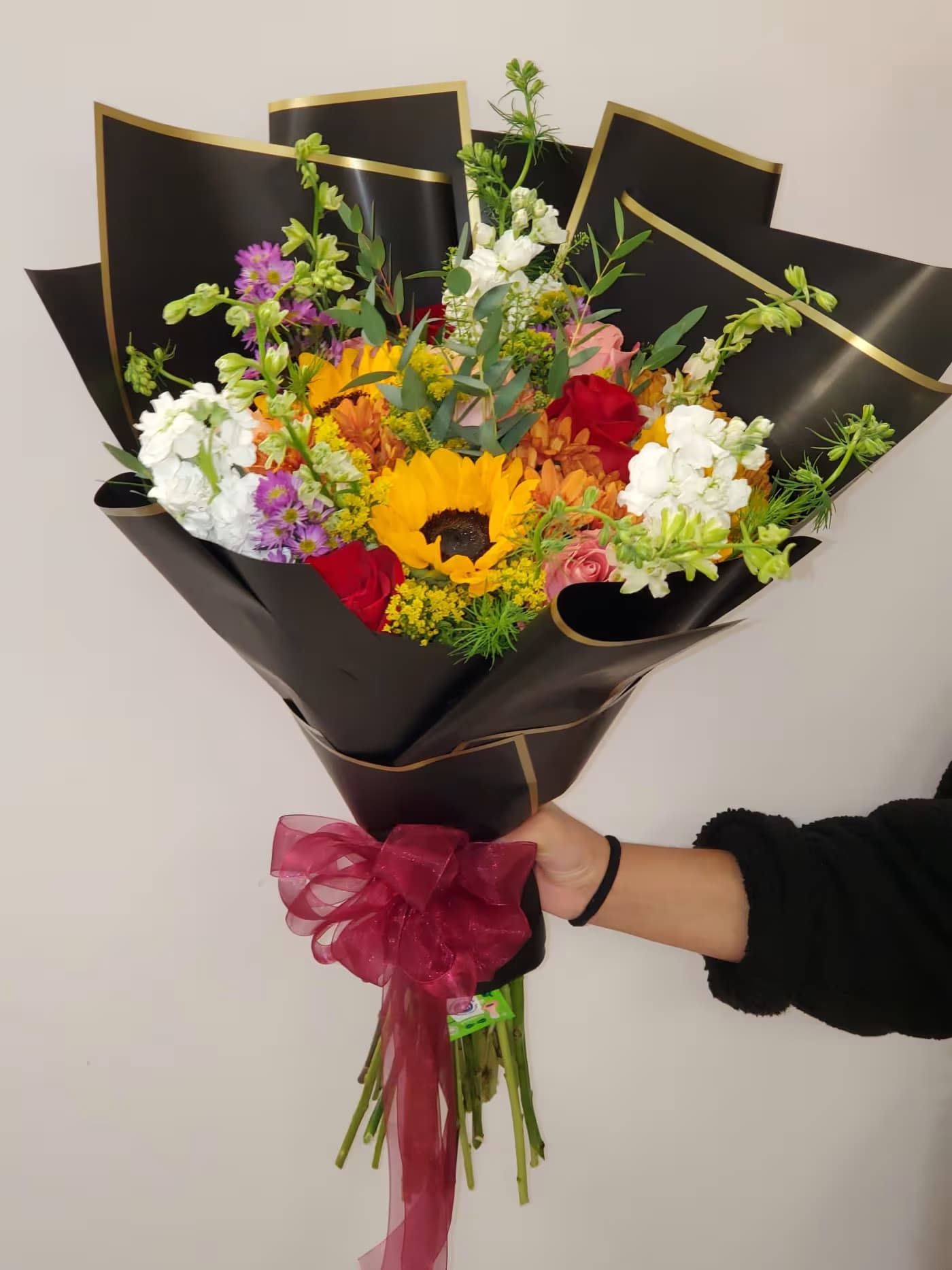 Mixed bouquet with a sunflower, roses, and white blooms wrapped in black paper