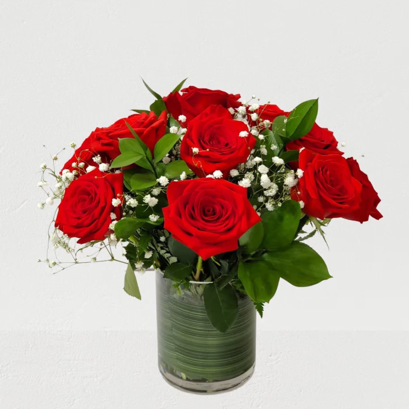 Red roses arranged in a glass vase with baby's breath and greenery