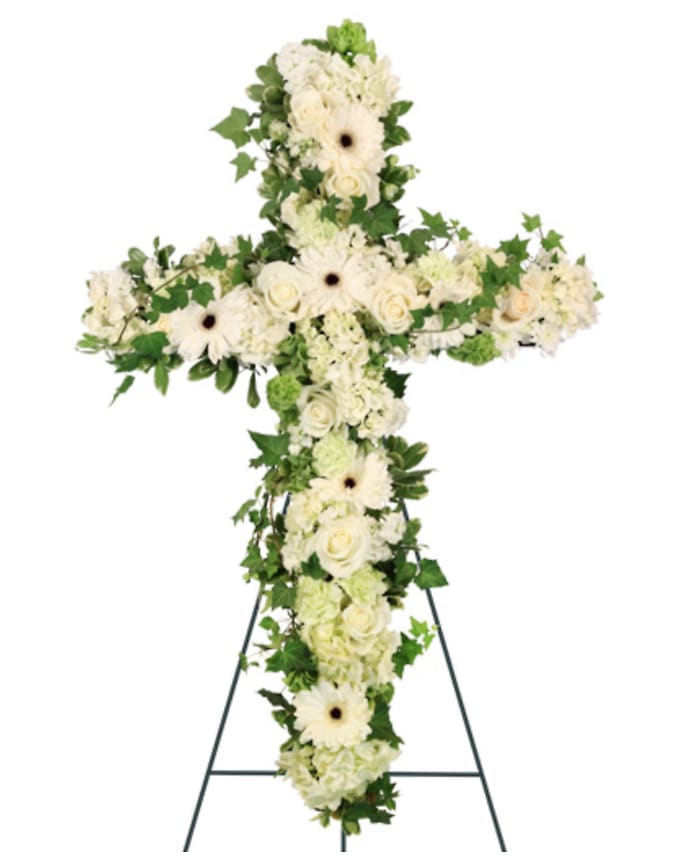 White floral cross on a stand with green foliage