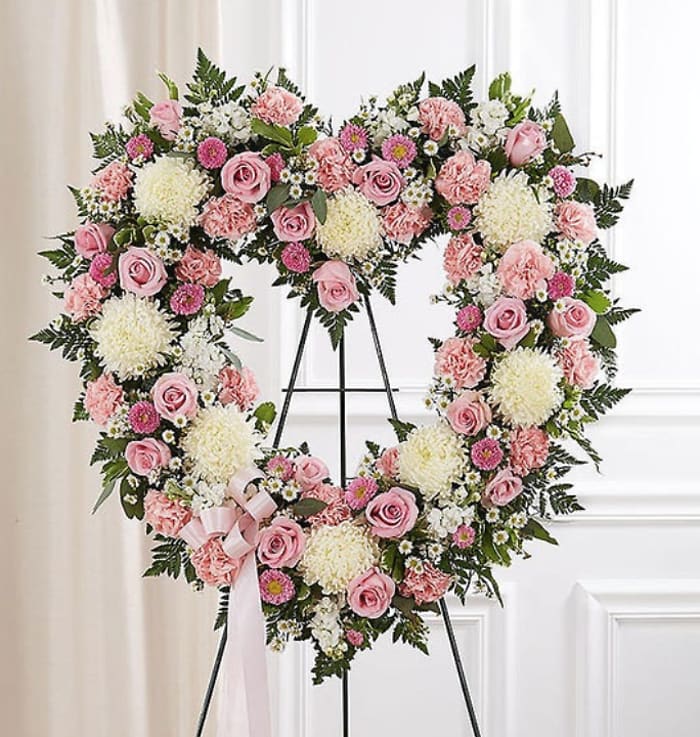 Heart-shaped floral wreath with pink roses and white blooms on a stand