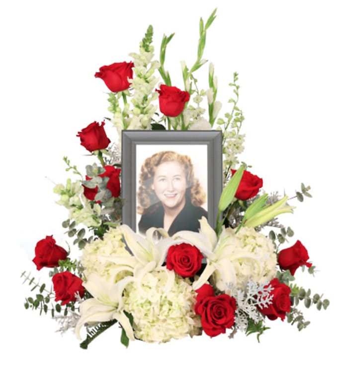 Memorial floral arrangement with red roses, white lilies, and a framed photo