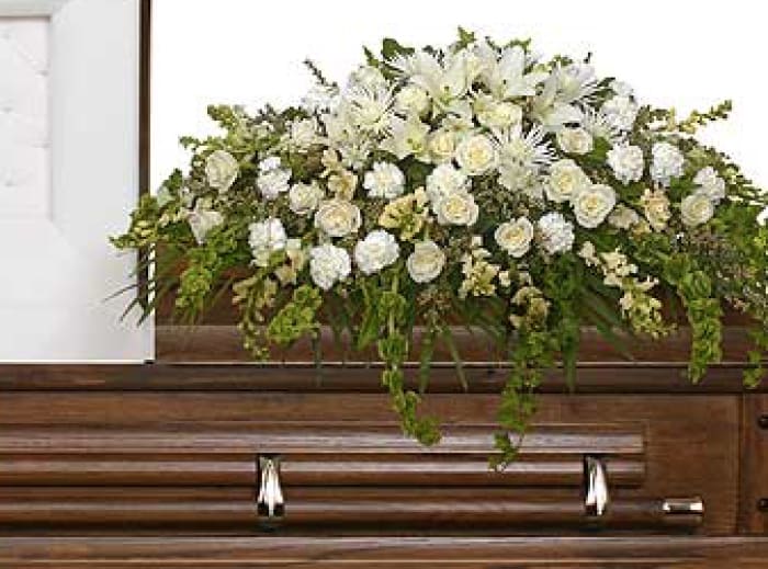White floral casket spray with trailing greenery on a wooden casket