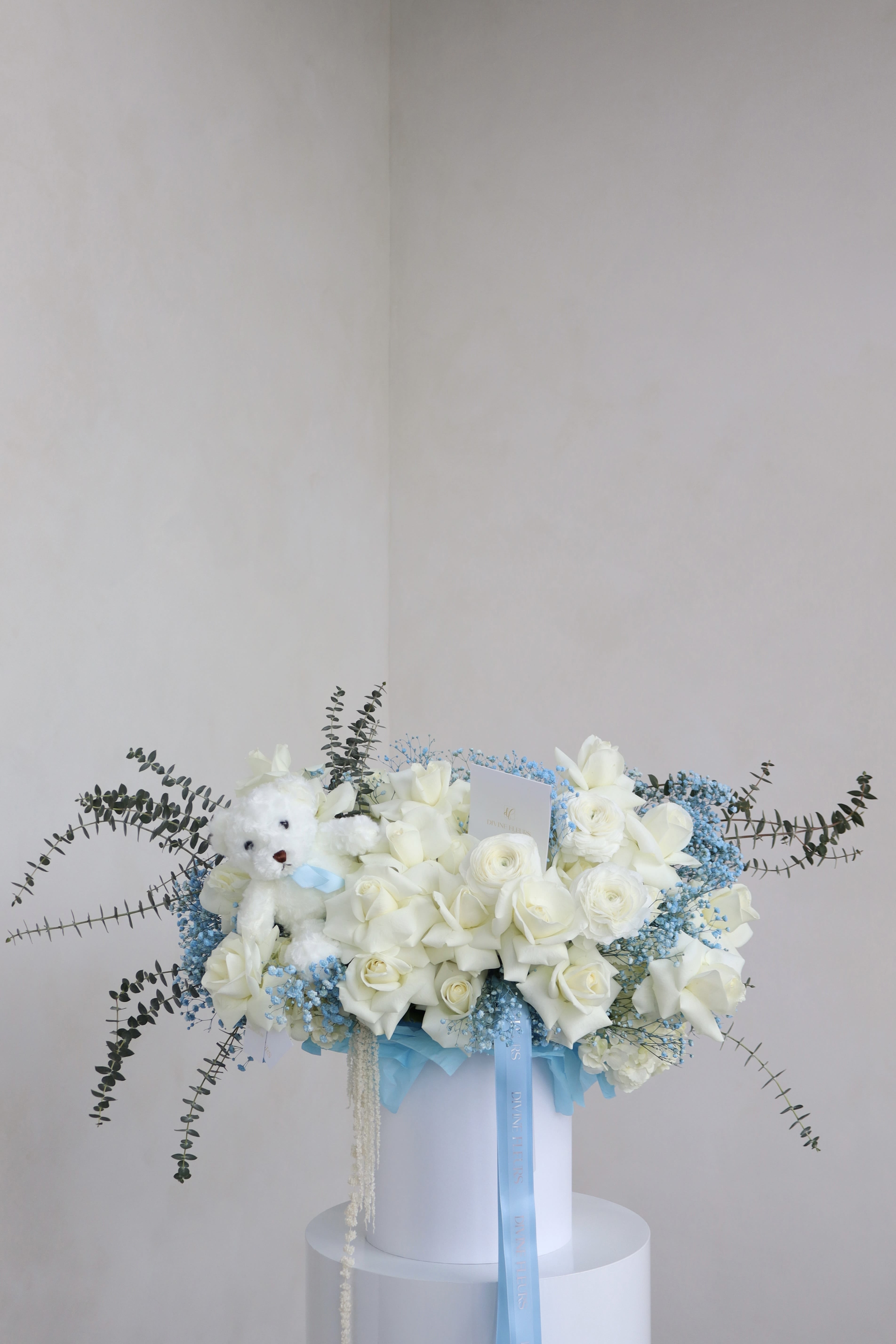 White rose bouquet with a teddy bear and blue ribbon in a white box