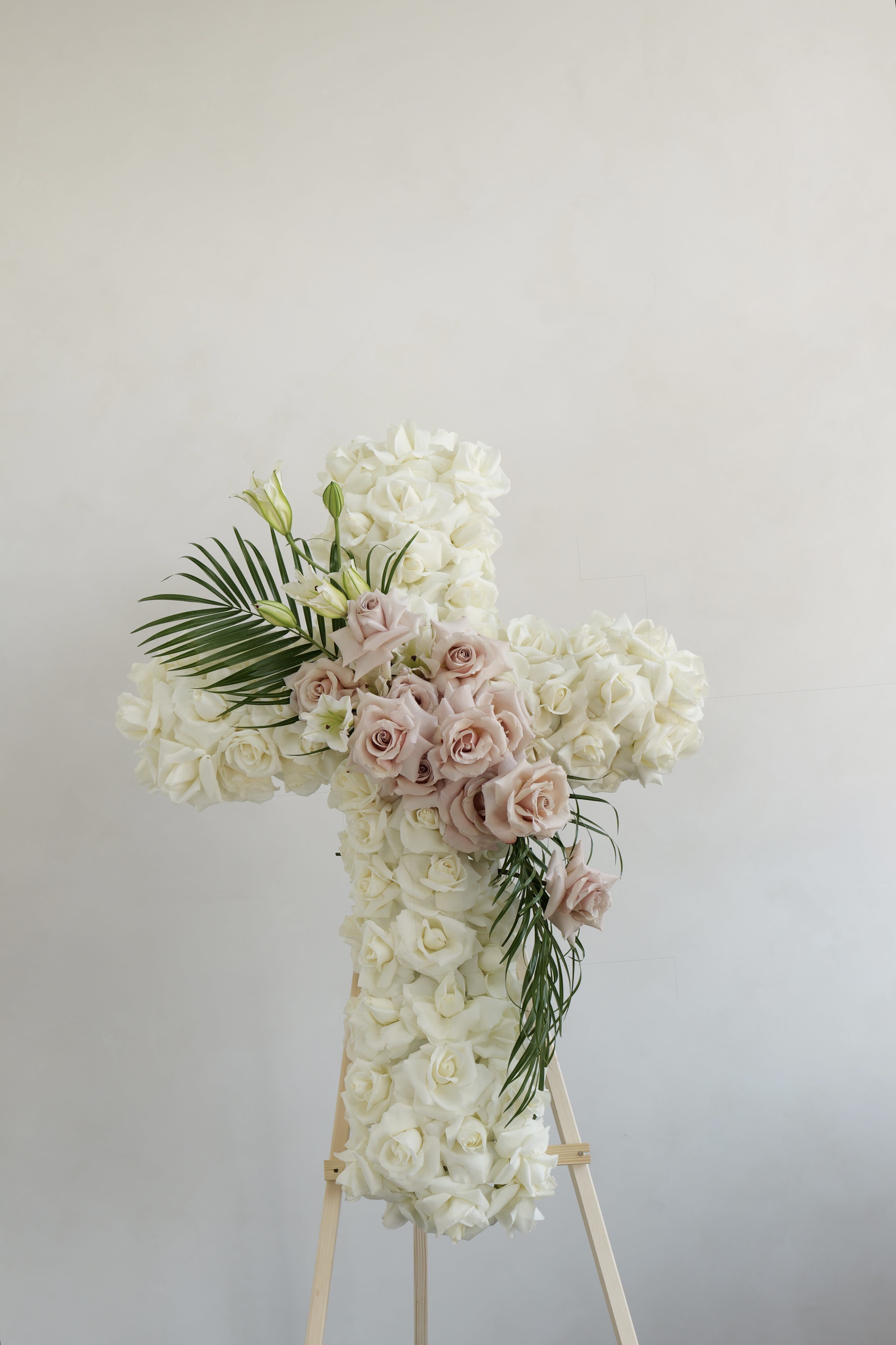 Cross-shaped floral arrangement of white and blush roses on an easel