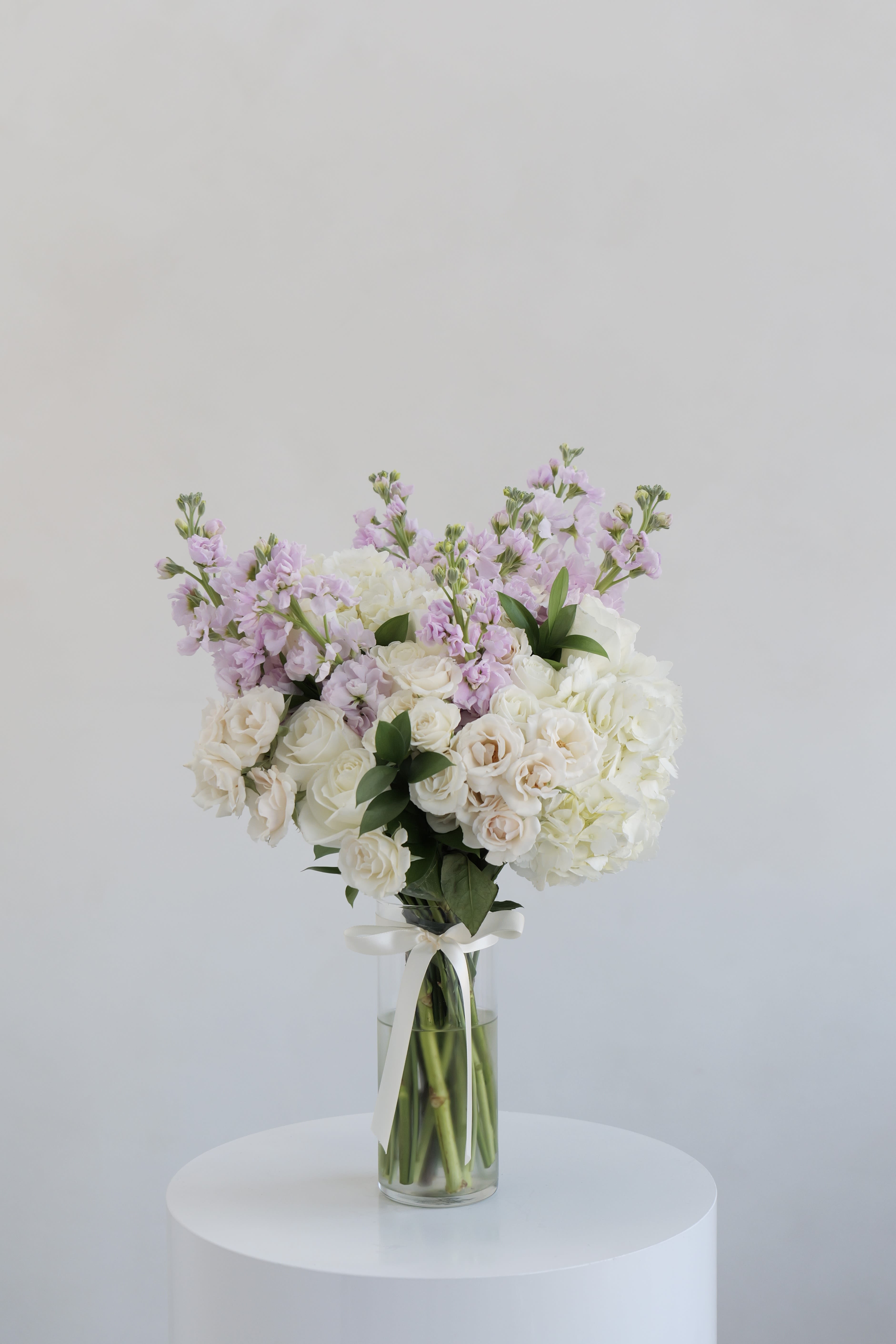 White and blush bouquet in a clear glass vase with a ribbon