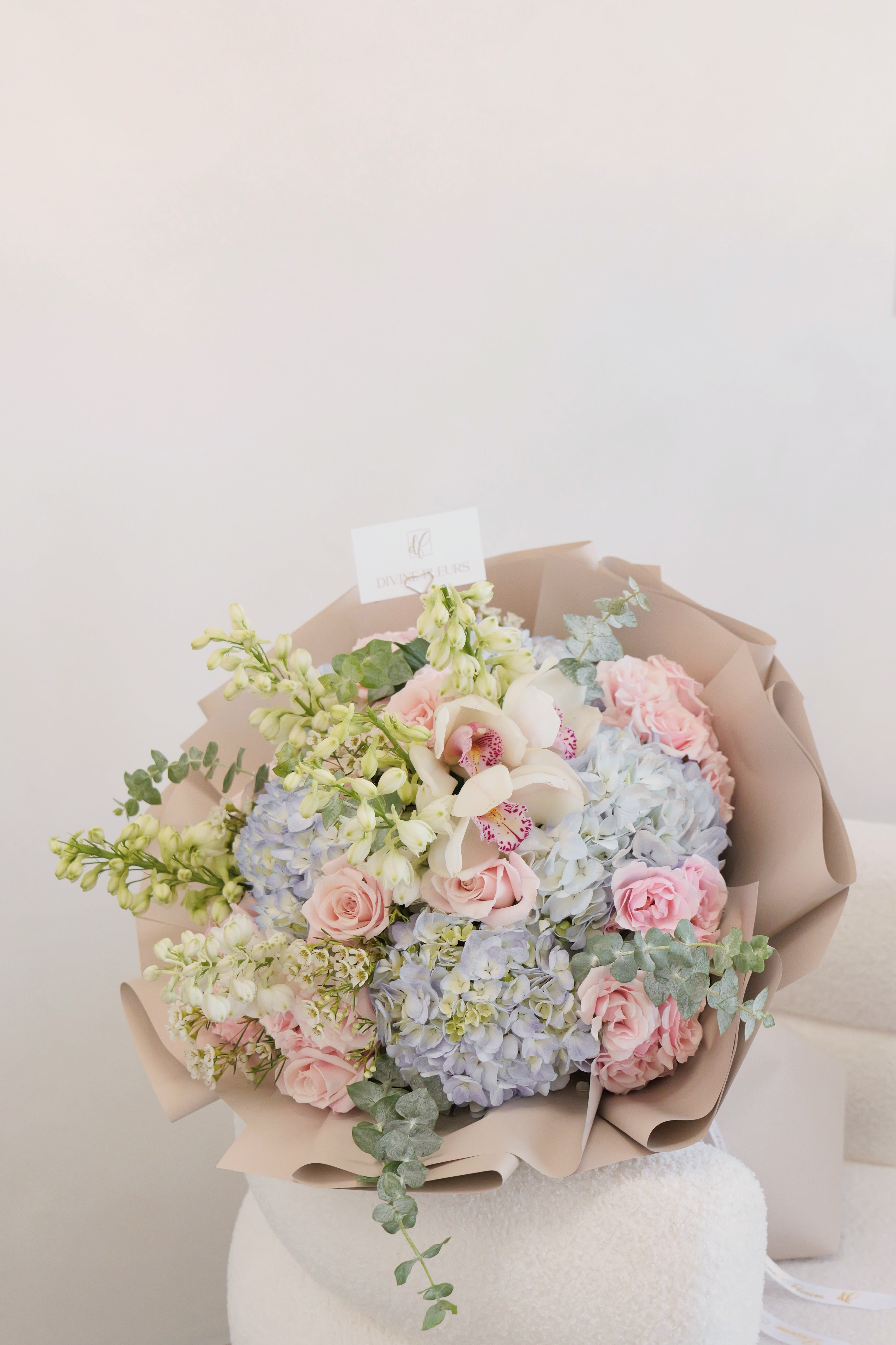 Pastel bouquet of pink roses, blue hydrangeas, and white orchids wrapped in beige paper