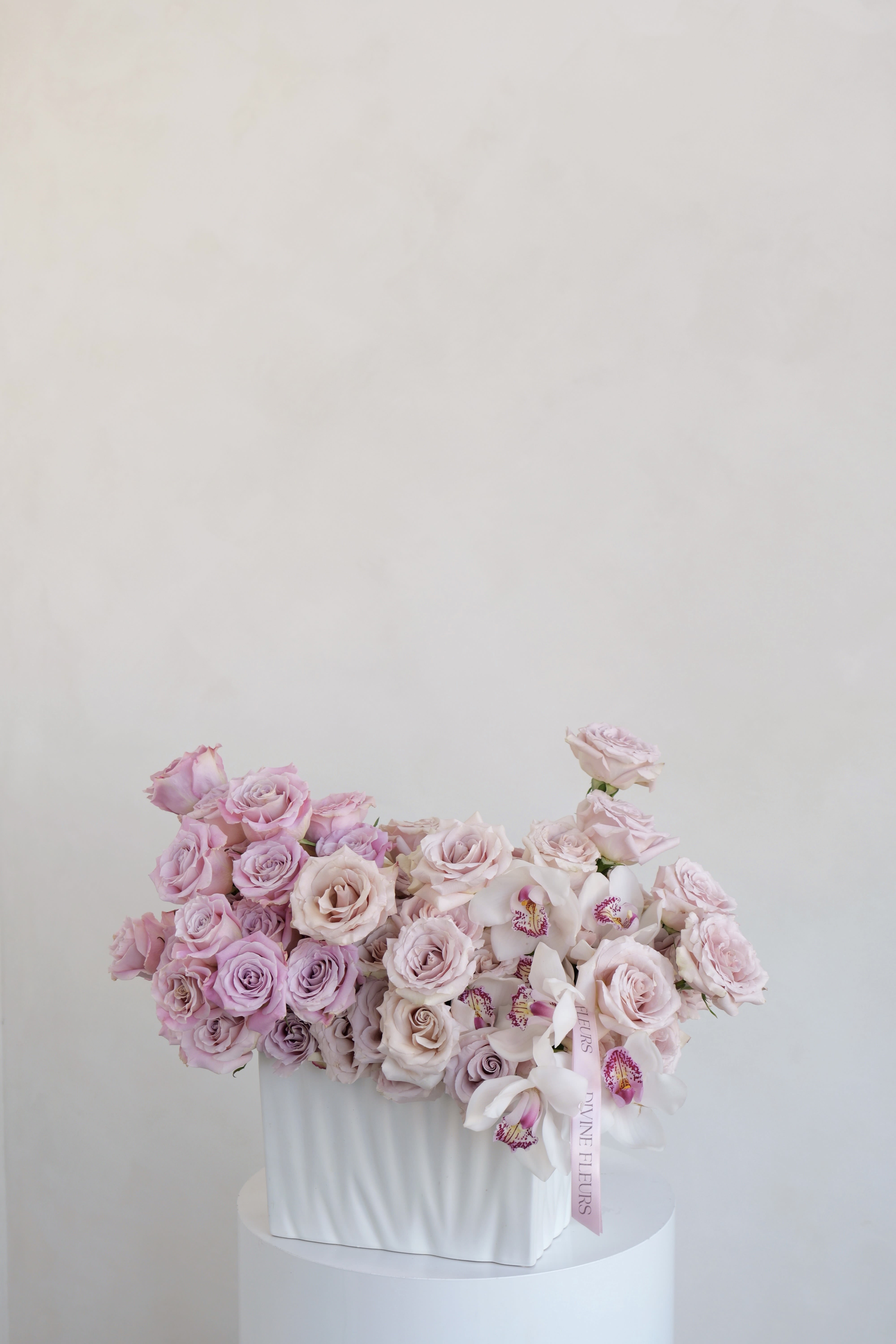 Pink roses and white orchids arranged in a white box