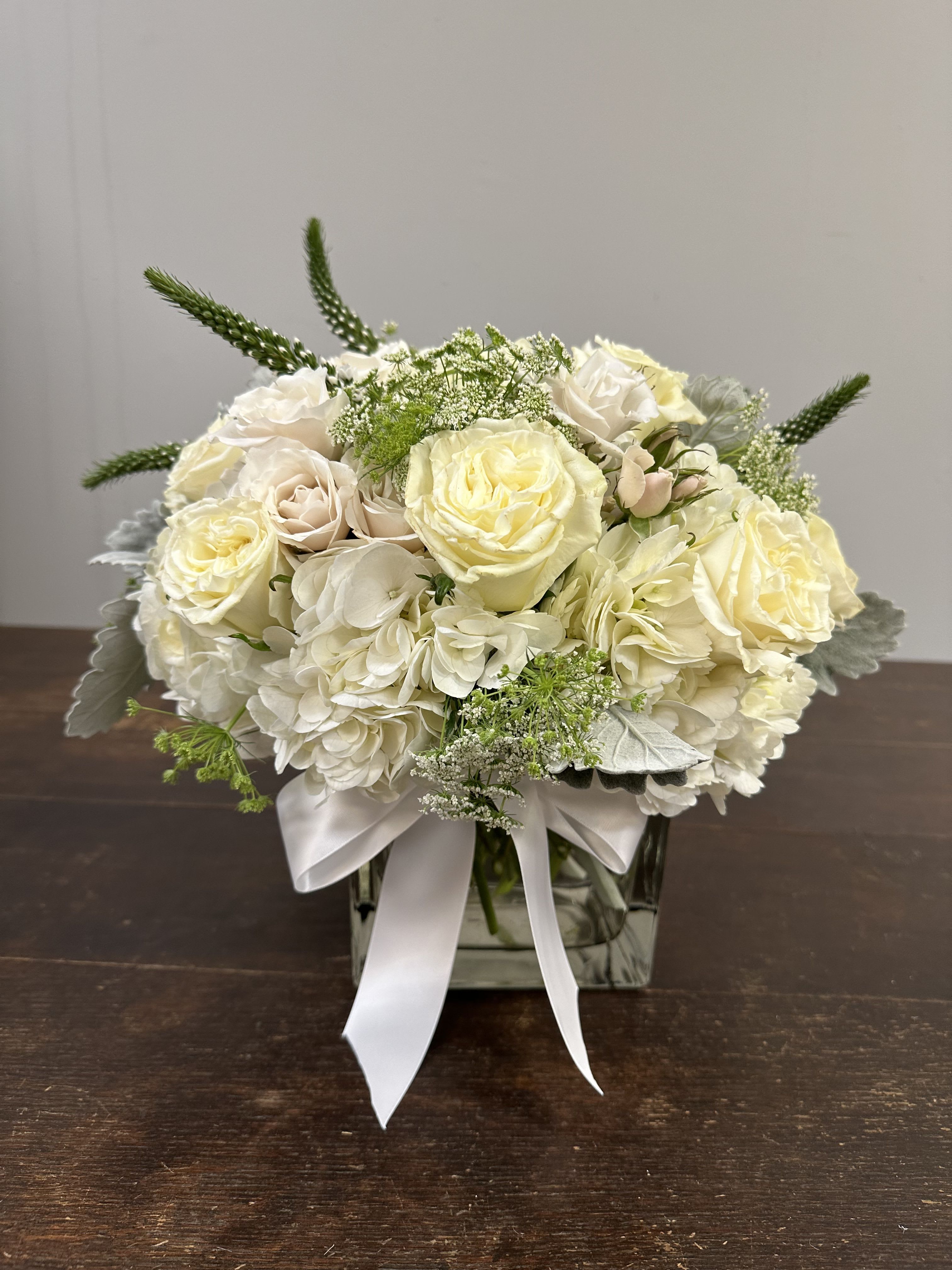 Cream rose and hydrangea arrangement in a square glass vase with a white ribbon