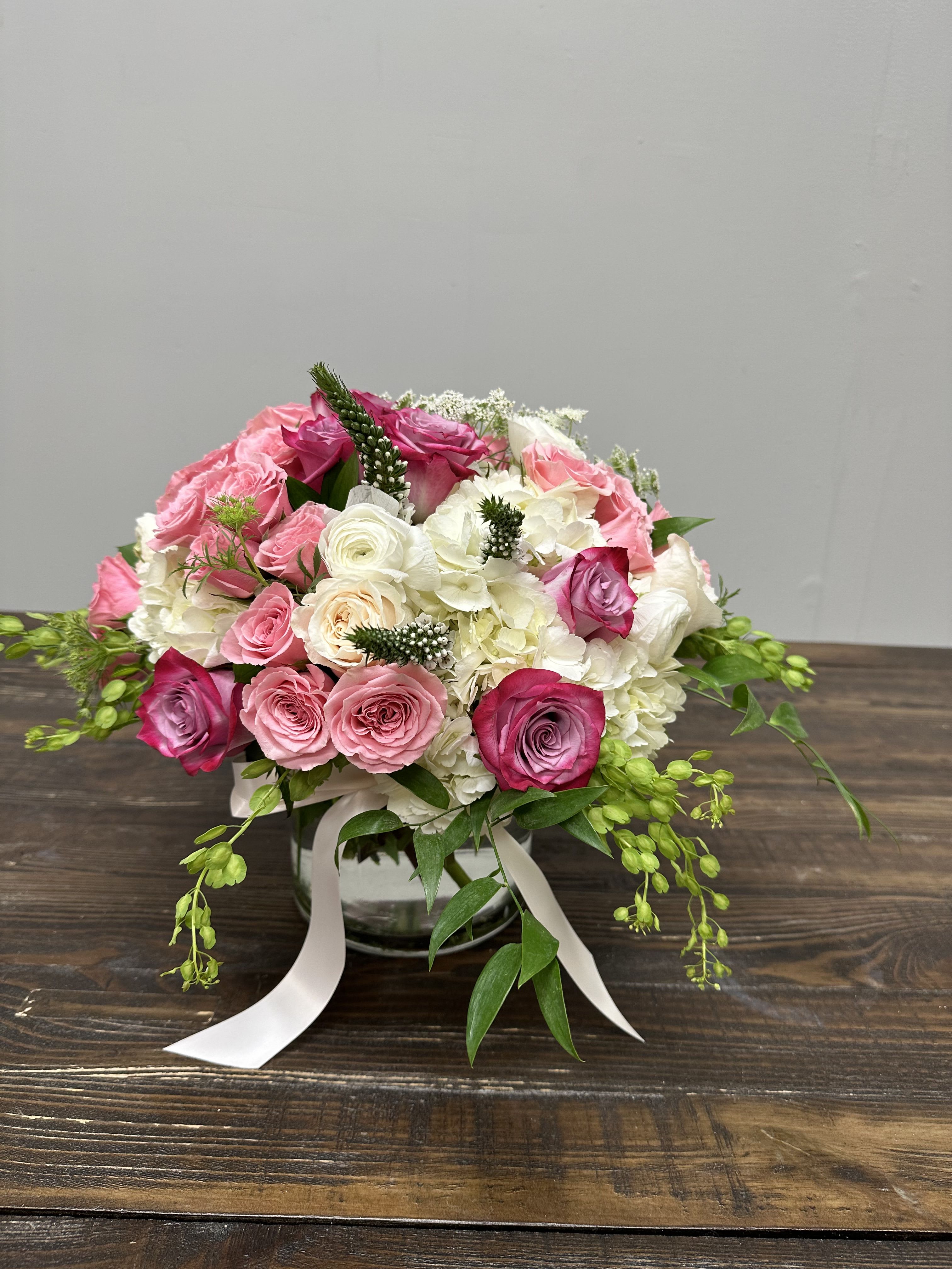 Pink and white rose bouquet in a glass vase with ribbon
