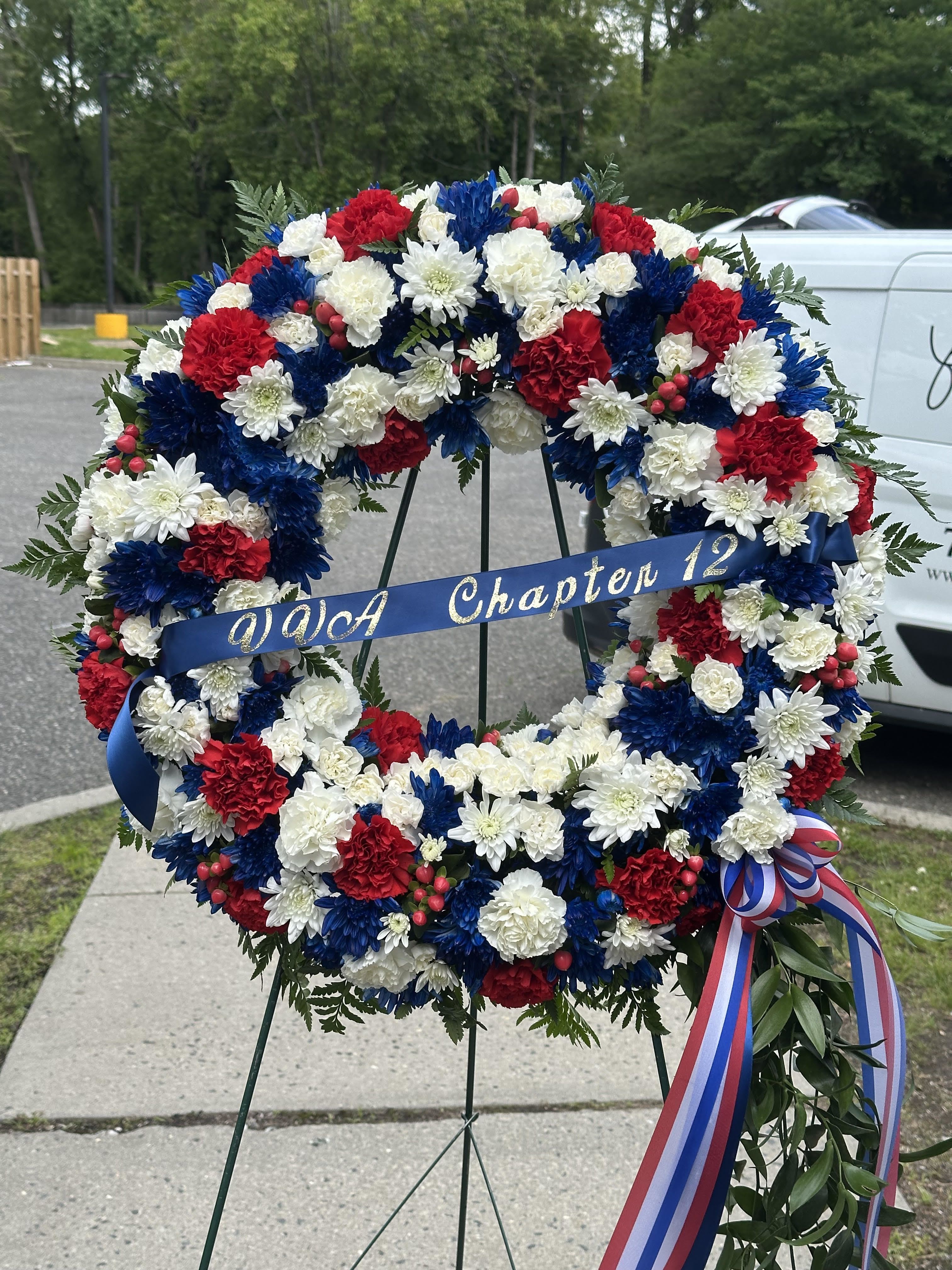 Red, white, and blue floral wreath on a stand with a ribbon