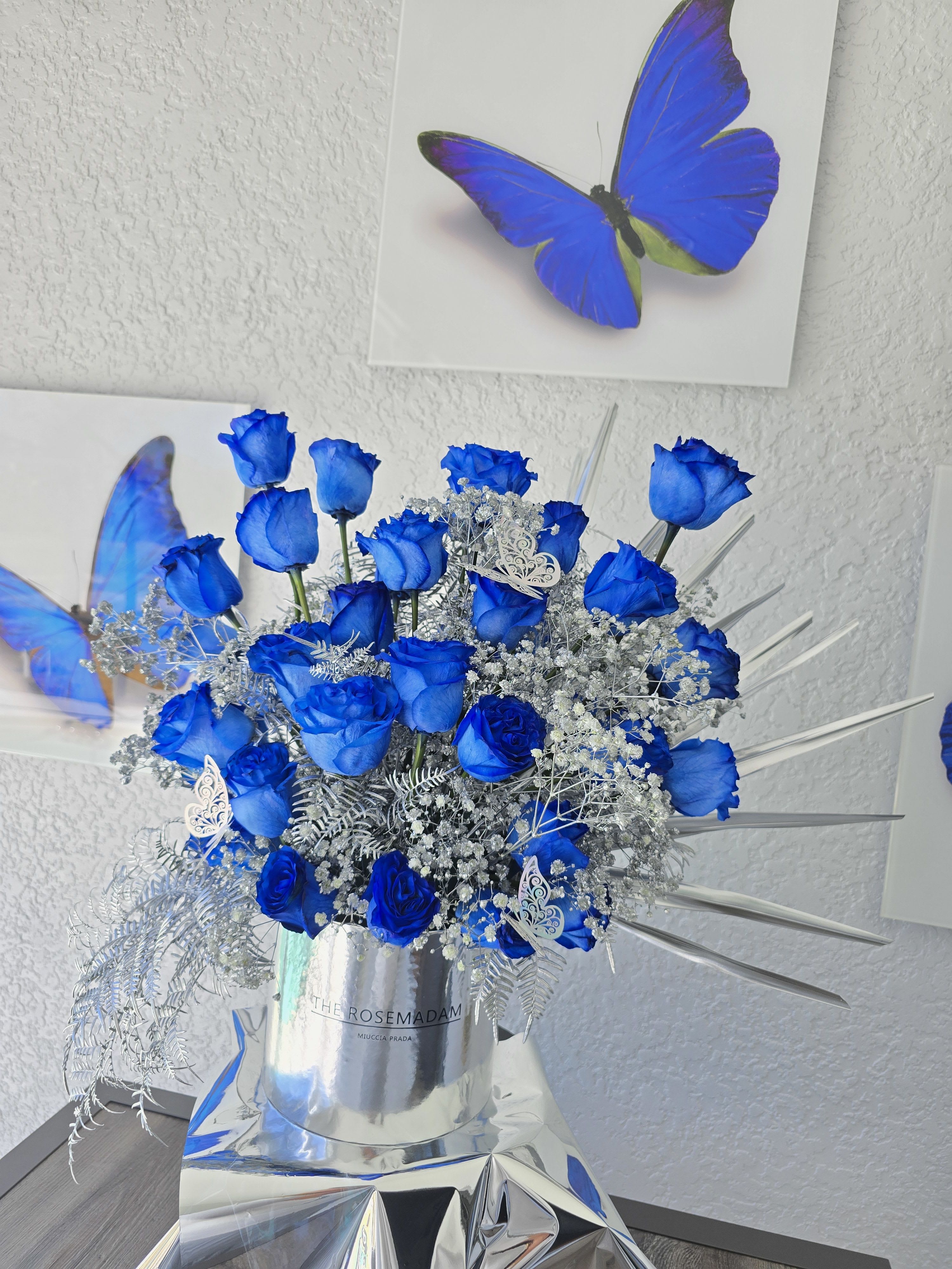 Blue Shine Arrangement - Serenity with a Touch of Glamour  Elegant and modern, our Blue Shine Arrangement features radiant blue-toned blooms paired with subtle metallic or shimmering accents. Designed to evoke peace, depth, and sophistication, it’s a perfect piece for refined spaces, thoughtful gifts, or unique celebrations.  Whether it’s for a special occasion or just because, this arrangement adds a calm yet striking presence to any room.   Delivery available  Cool tones. Elegant glow. Effortlessly beautiful.
