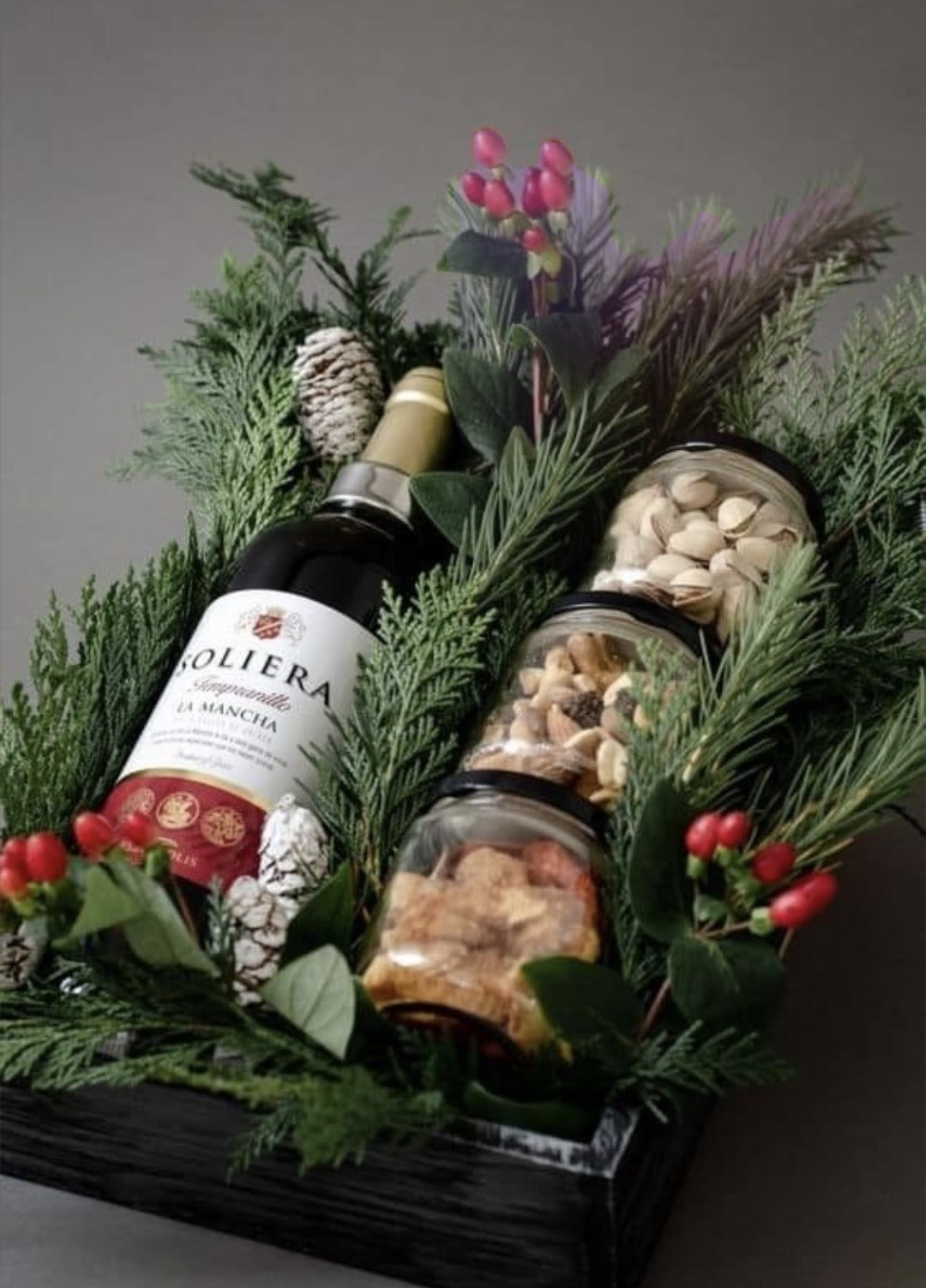 Gift basket with wine, jars of nuts, and evergreen sprigs