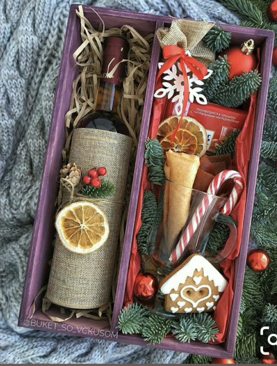 Holiday gift box with a wine bottle, candy cane, cookie, and ornaments