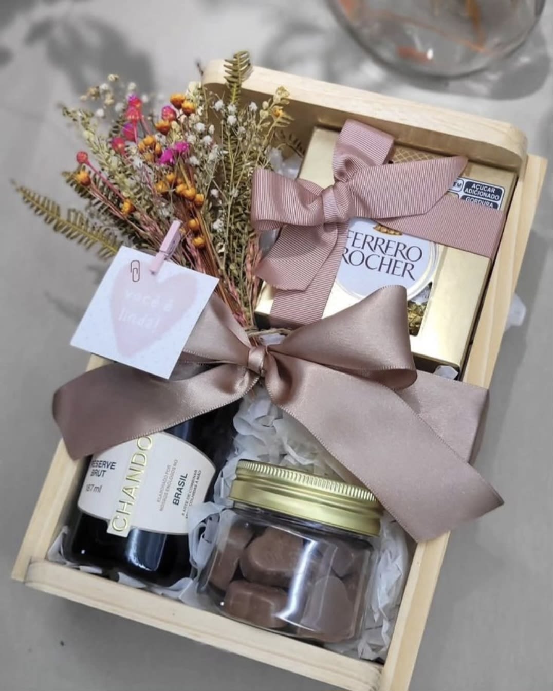 Gift box with dried flowers, chocolates, and a bottle of wine tied with pink ribbon