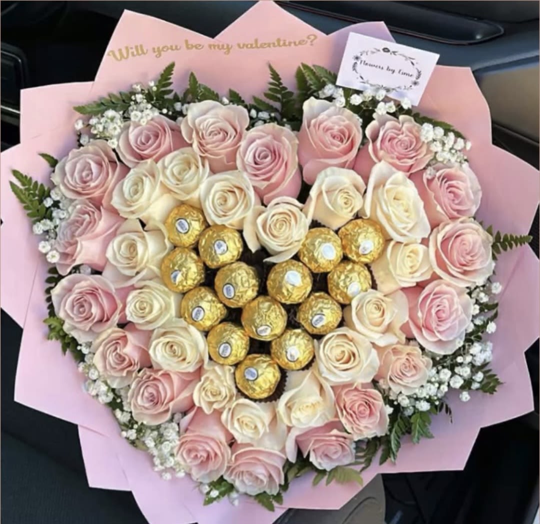 The Pastel Heart Masterpiece - A symphony of tenderness and luxury. This stunning hand-tied bouquet features a romantic heart-shaped arrangement of premium blush pink and creamy white roses. At its center, a decadent cluster of golden Ferrero Rocher chocolates adds a sweet touch of gold. A truly sophisticated work of art from Hopes Gallery,