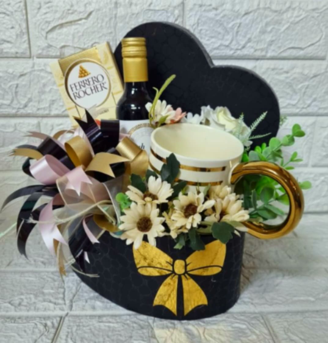 The "Midnight &amp; Gold" Gentleman's Box - A stylish black heart-shaped box featuring a luxury gold-rimmed mug, a mini bottle of fine wine, and premium Ferrero Rocher chocolates. Accented with fresh white daisies, eucalyptus, and a striking black and gold multi-layered bow, it’s the perfect compact luxury gift for Dad.  