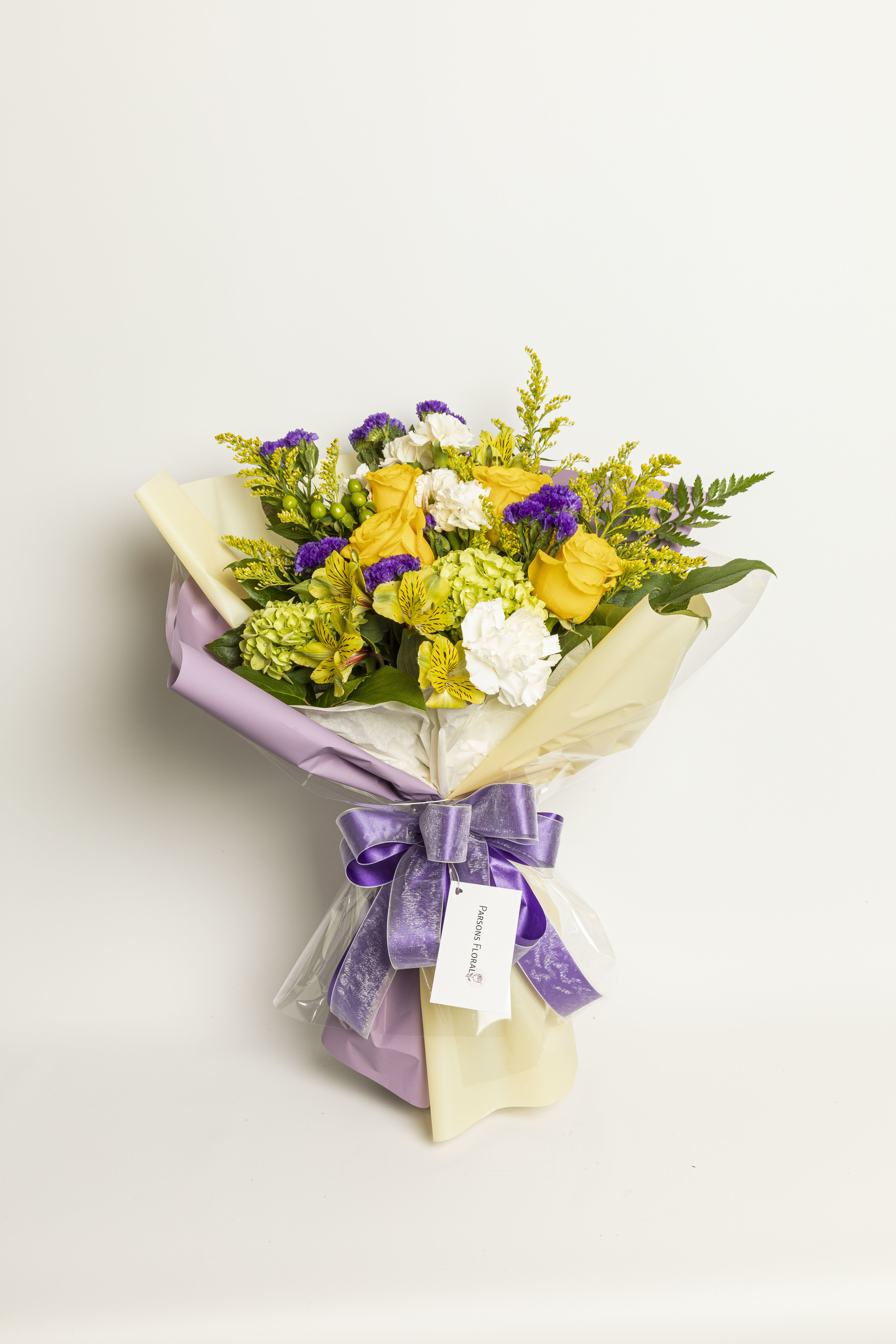 Yellow roses and white flowers in a wrapped bouquet with a purple ribbon