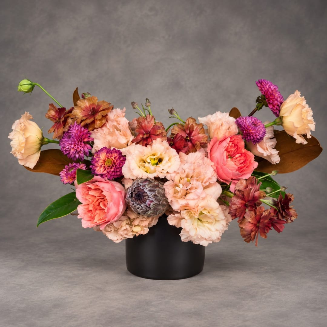 Mixed pink and peach flowers arranged in a black vase
