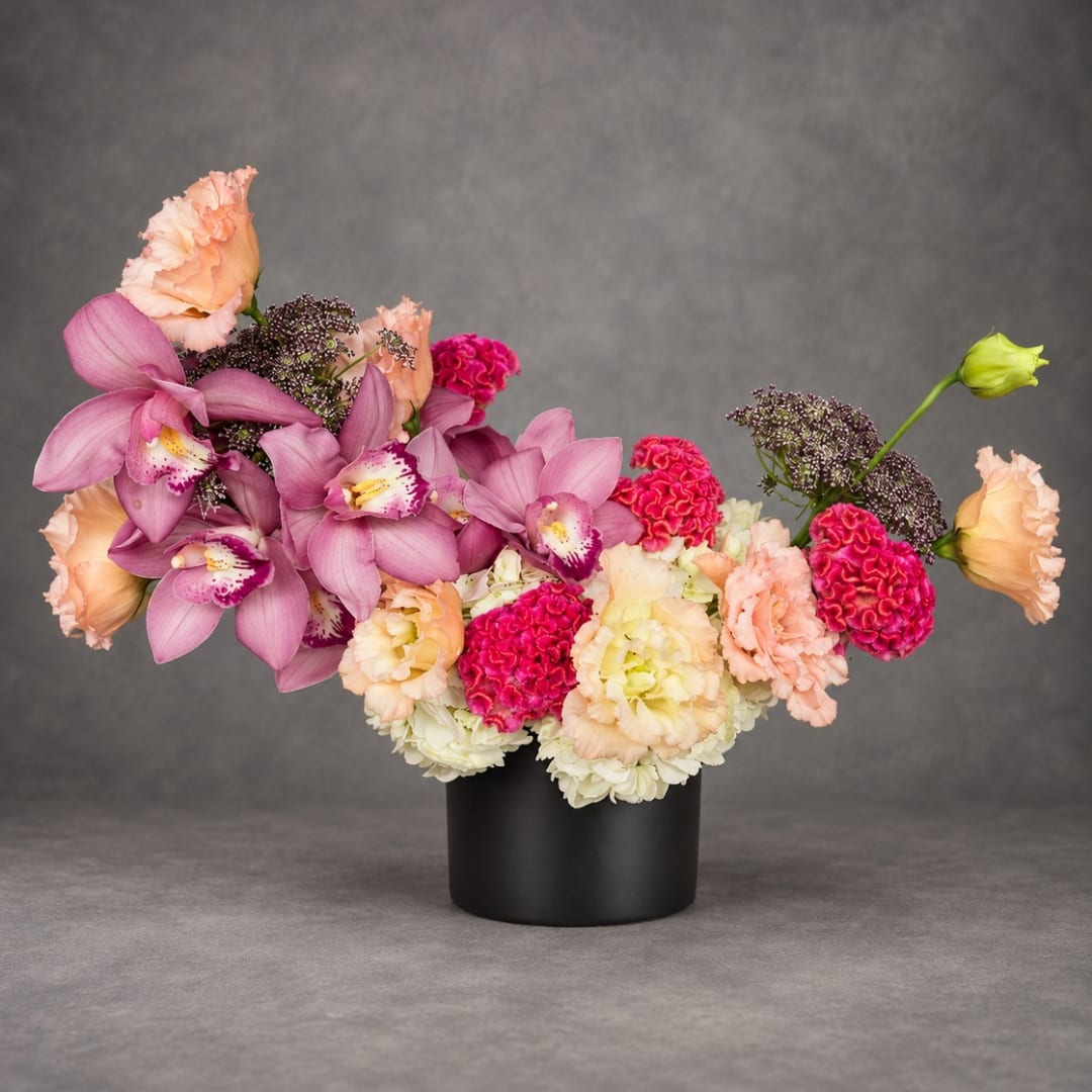 Pink orchids and peach carnations arranged in a black vase