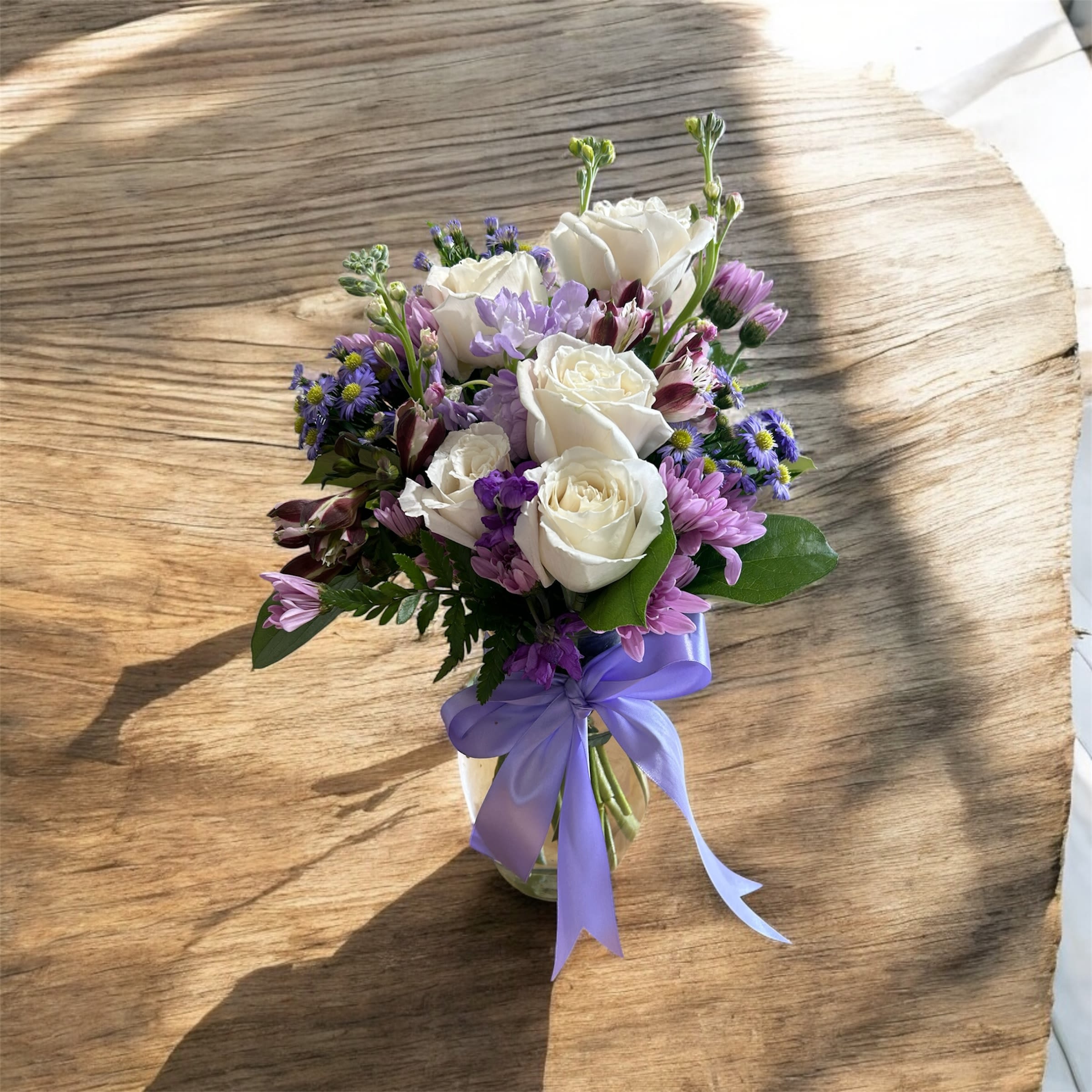 Small vase arrangement of white roses and purple flowers with a lavender ribbon bow