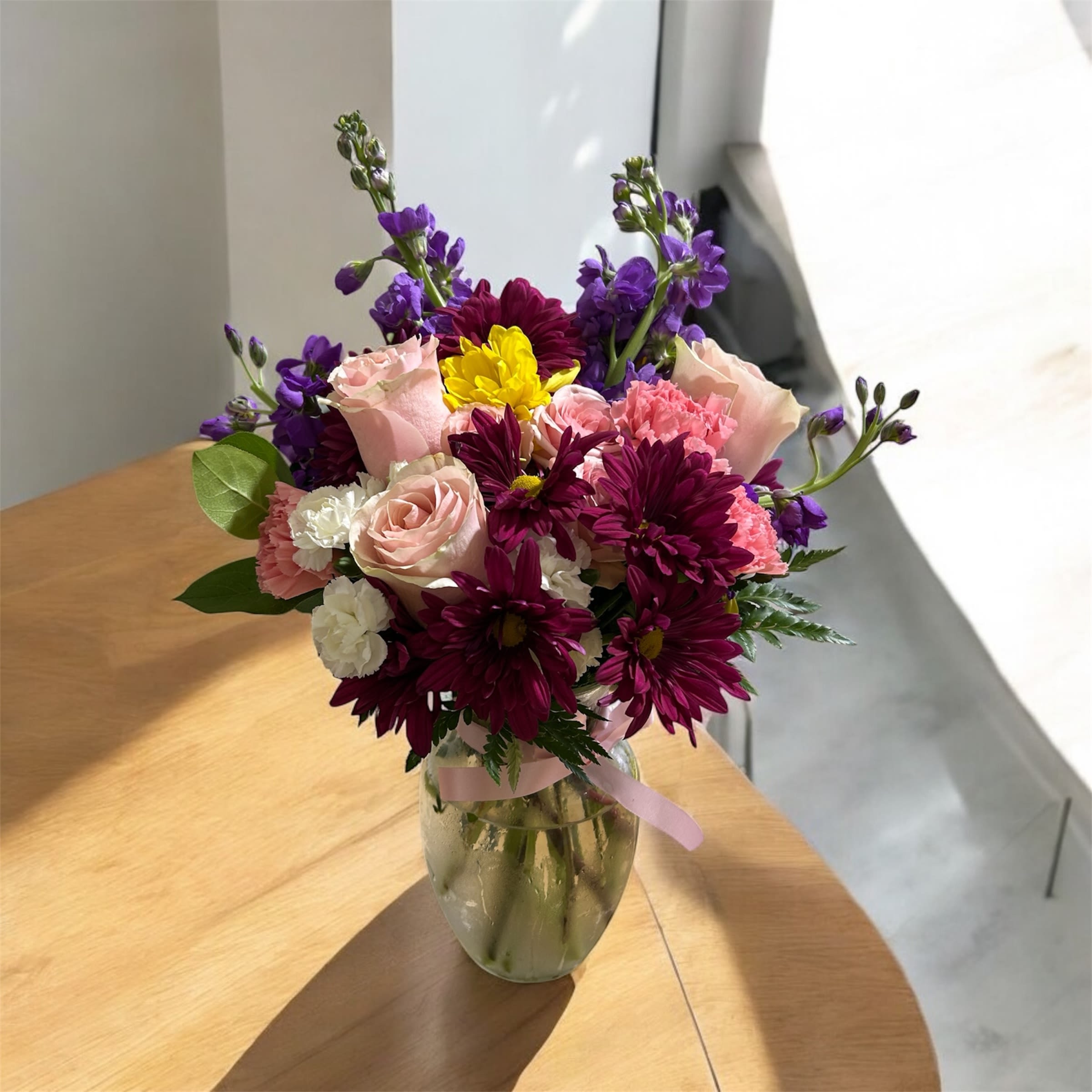 Mixed bouquet of pink, purple, and yellow flowers in a glass vase