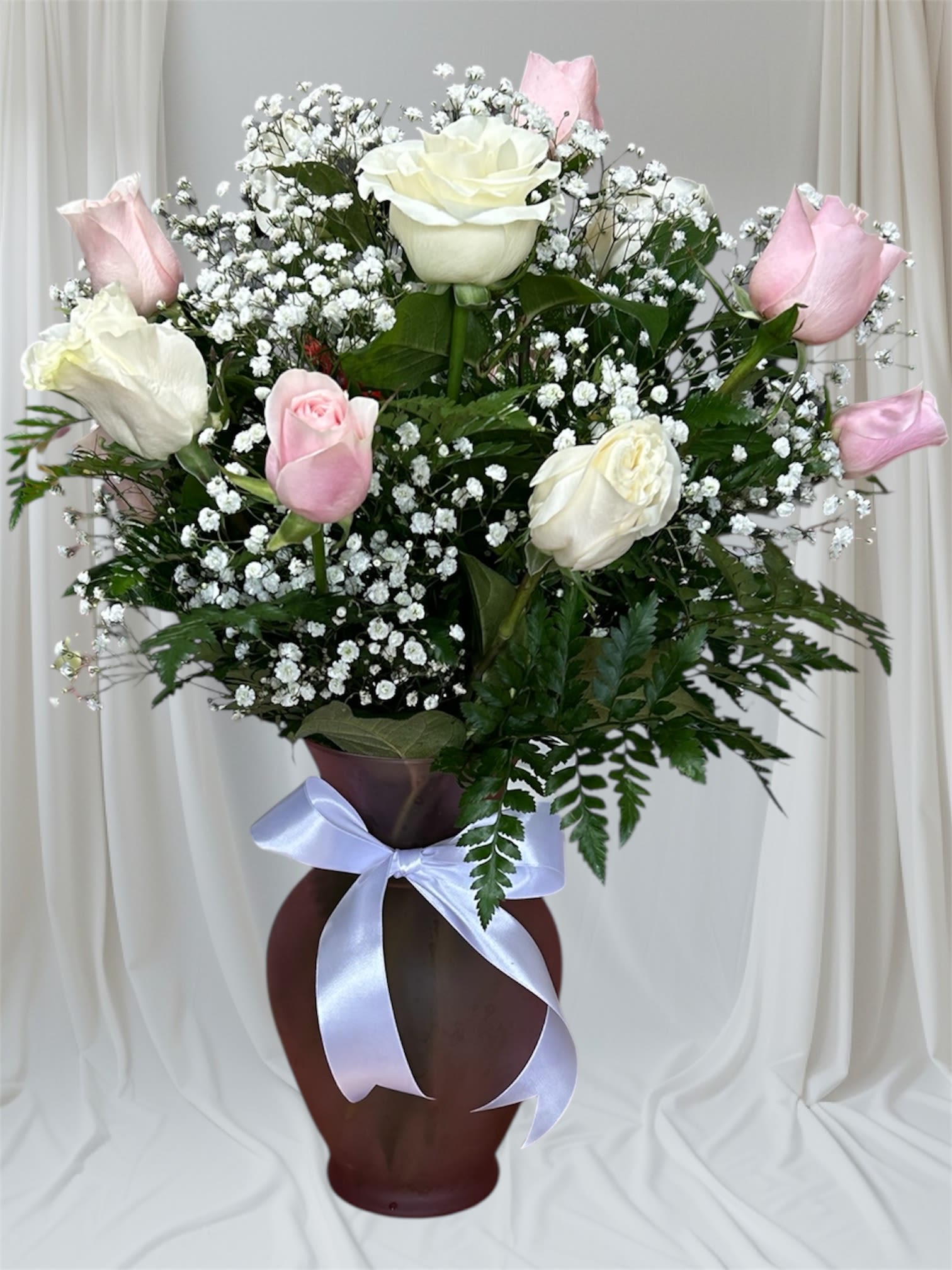 Pink and white roses arranged in a tall vase with baby's breath