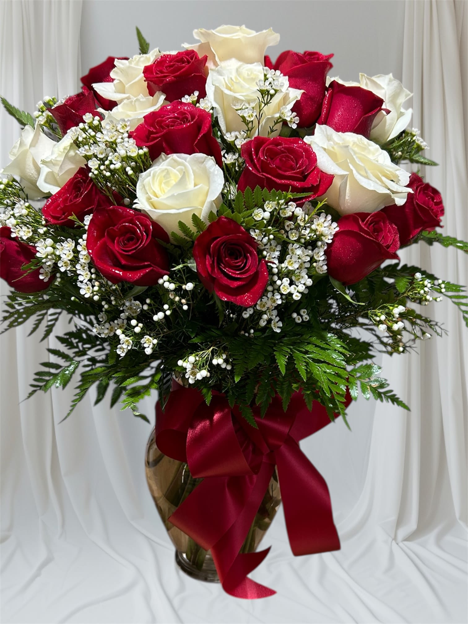 Red and white roses arranged in a glass vase with a red ribbon