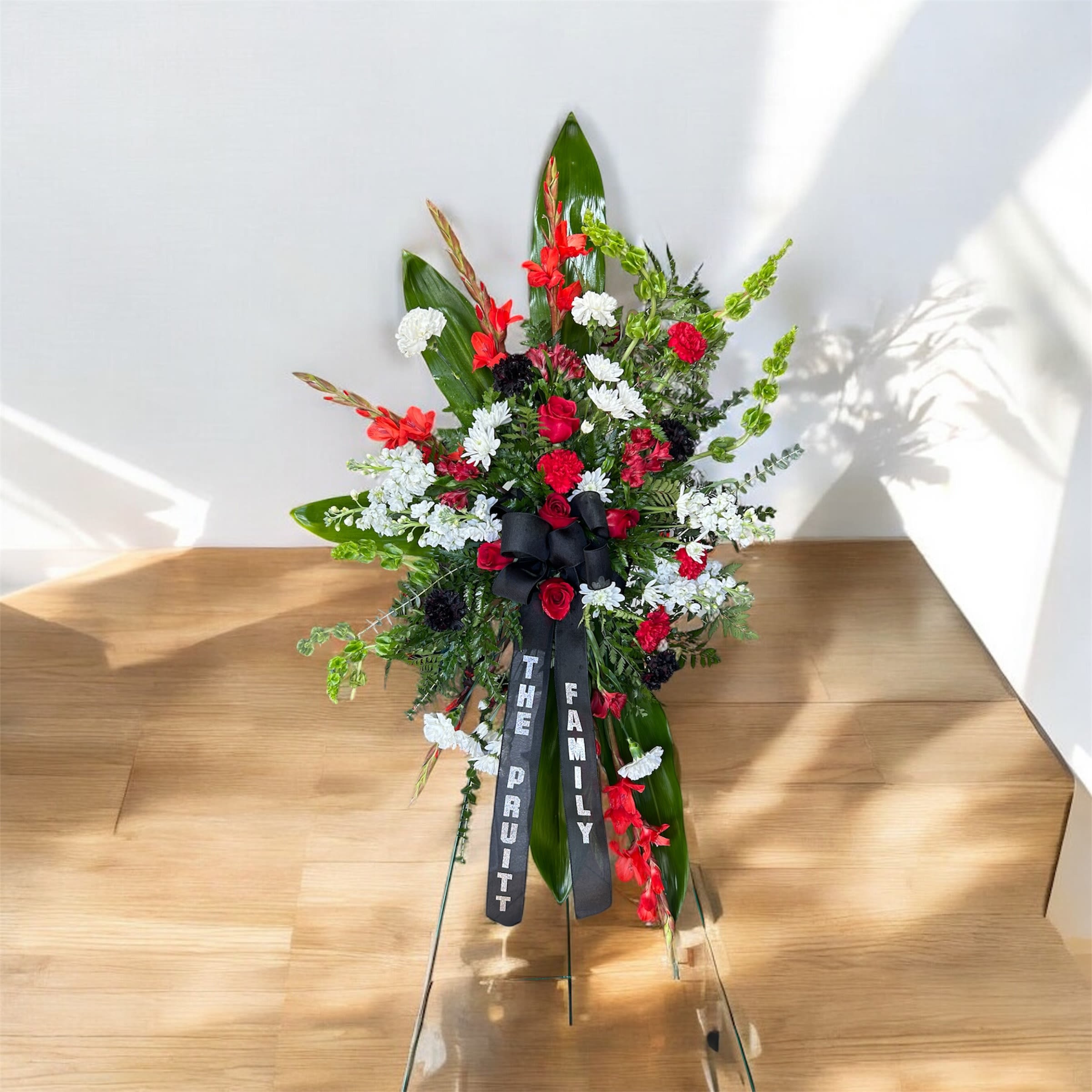 Tall floral standing spray with red, white, and black flowers and a black ribbon