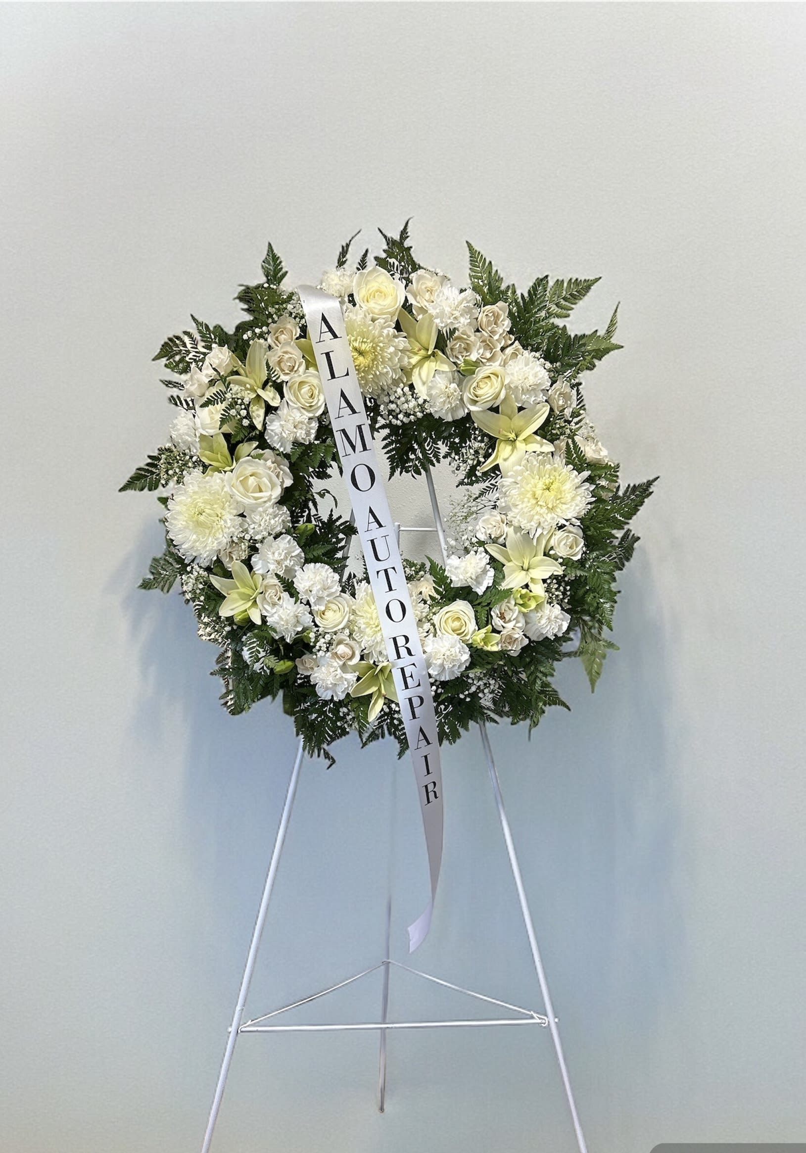 White funeral wreath on a stand with roses and lilies