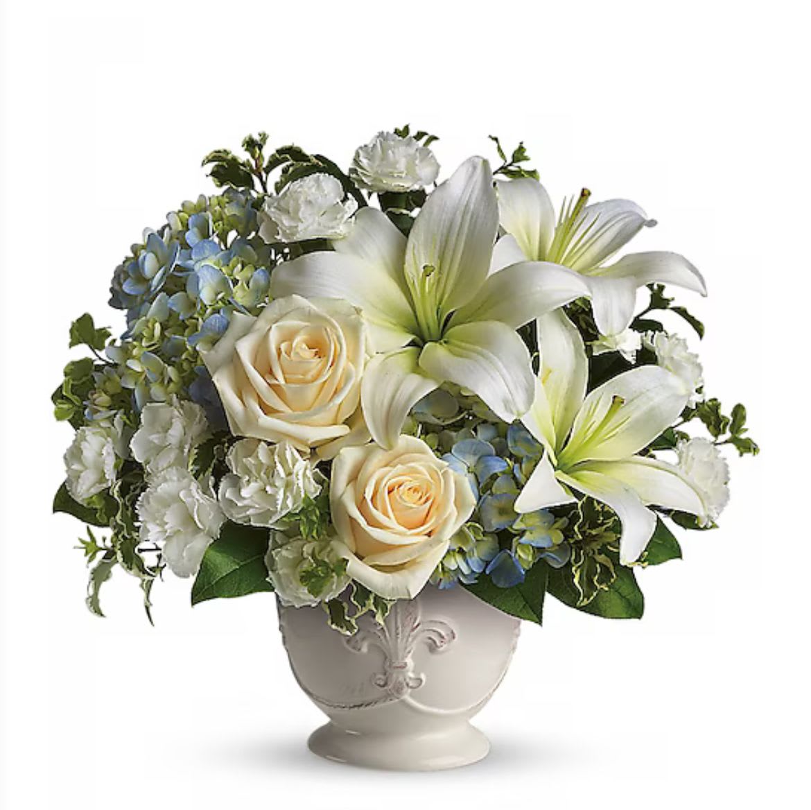White lilies, cream roses, and blue hydrangeas arranged in a white ceramic urn-style vase