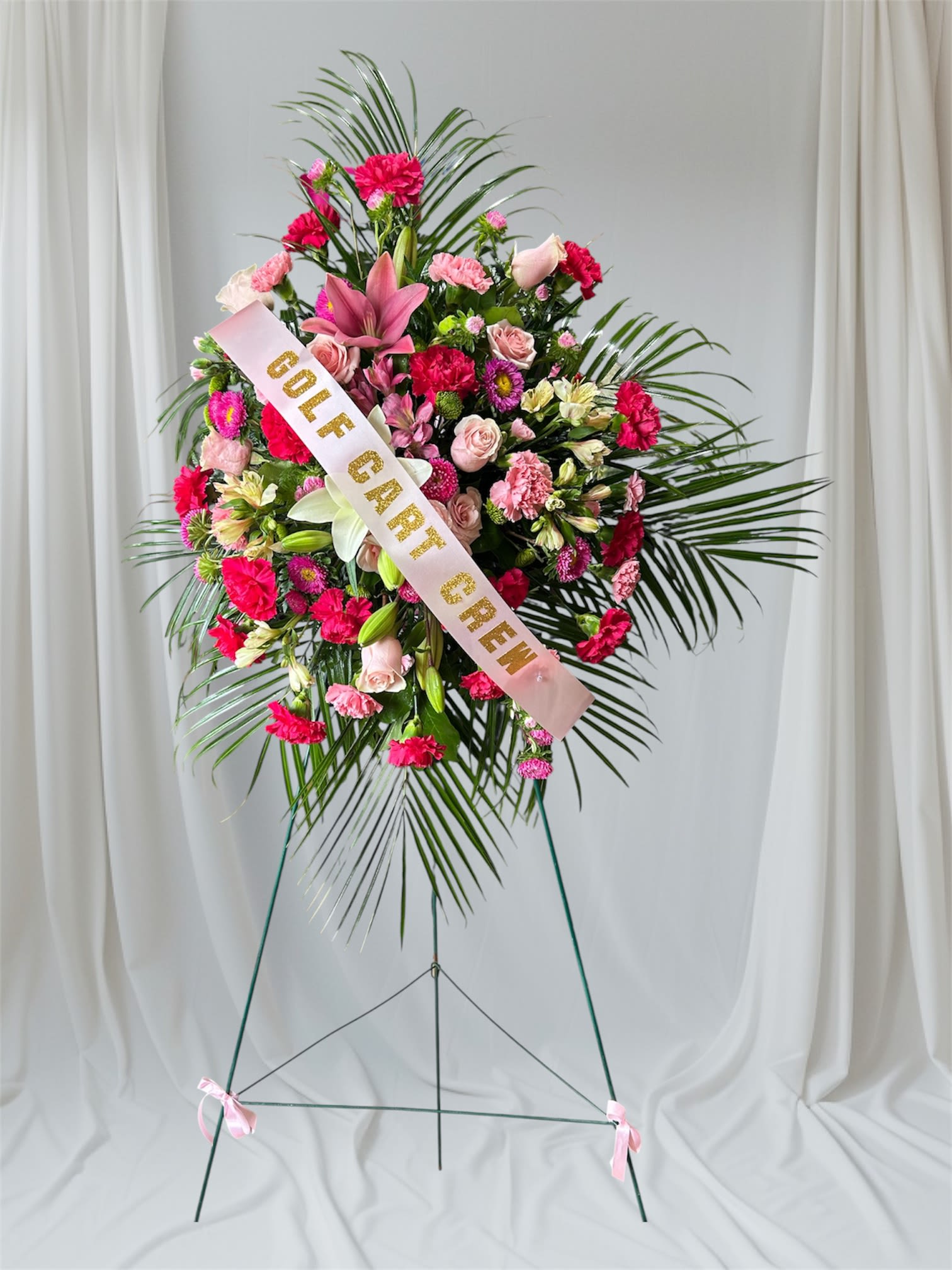 Standing floral wreath with pink flowers and a gold-lettered ribbon
