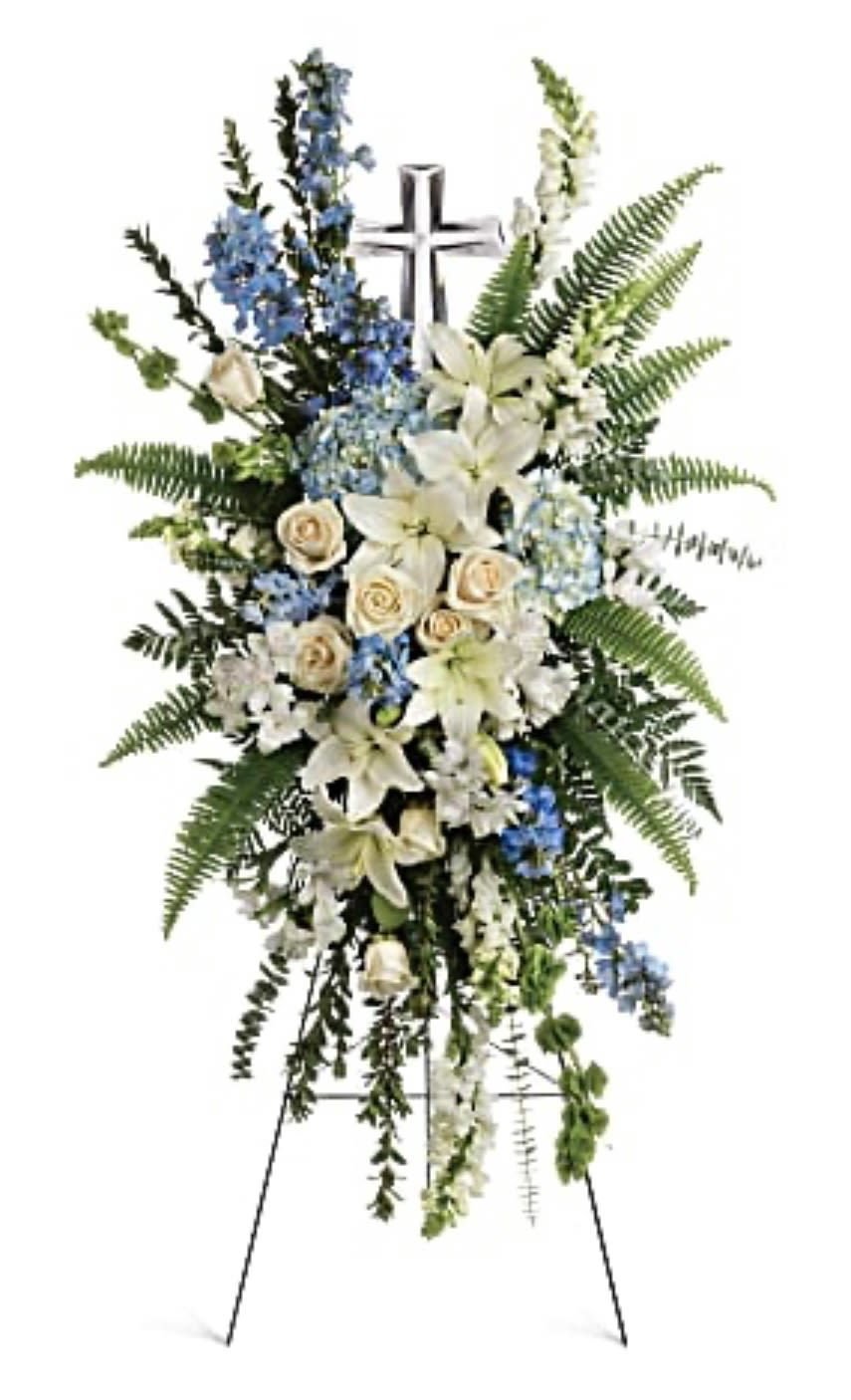 Standing funeral spray with white lilies, cream roses, and blue flowers on an easel