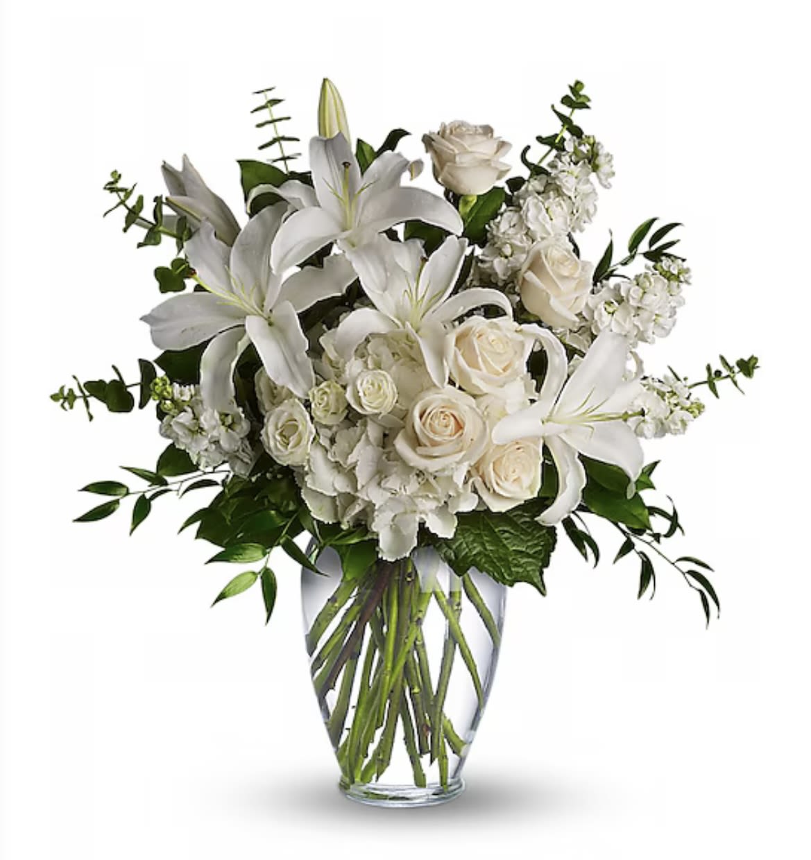 White lilies and roses with other white blooms arranged in a clear glass vase