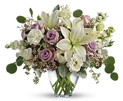 Pastel bouquet of white lilies and lavender roses arranged in a clear glass vase