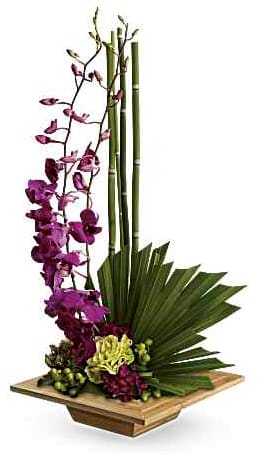 Tall floral arrangement with purple orchids and bamboo in a wooden base