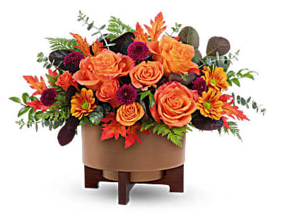 Orange roses and autumn flowers in a round vase on a wooden stand