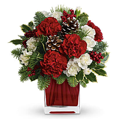 Red and white floral arrangement in a clear square vase with pinecones and berries