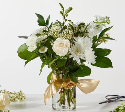 White and cream flowers in a clear glass vase with a gold ribbon bow