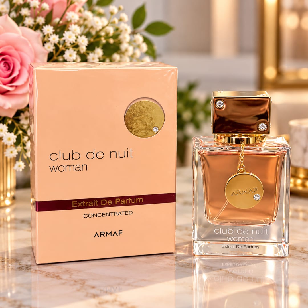 Perfume bottle and box beside pink roses and small white flowers