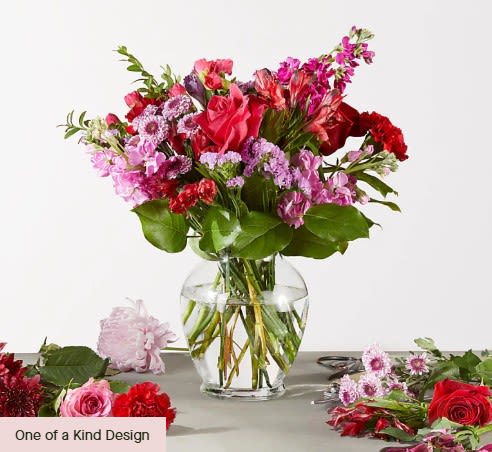 Regal Jewel - A generous, garden-inspired arrangement that reads romantic and joyful-perfect as a birthday bouquet, anniversary flowers, or a cheerful "thinking of you" gift. The mix of pinks and reds with lavender and white accents gives the Regal Jewel a lively, feminine presence that will make the person you're sending it to feel truly celebrated.  This full, rounded display pairs rose-like focal blooms with alstroemeria, carnations, dianthus, asters, stock, lilies, daisies and assorted filler flowers for layered texture and depth. Bright magenta and hot-pink pops mingle with softer blush and white tones, all set against green foliage for contrast. Arranged in a clear glass vase with visible stems in water, the design reads fresh and casually elegant-an abundant, loose garden-style shape with taller stems and airy sprays creating movement.  Send this when you want to mark a milestone or simply brighten someone's day: it suits birthdays, anniversaries, thank-you moments, or just-because surprises. The vase-ready presentation arrives ready to display; for best longevity, keep stems in fresh water, out of direct sun, and recut stems if needed.
