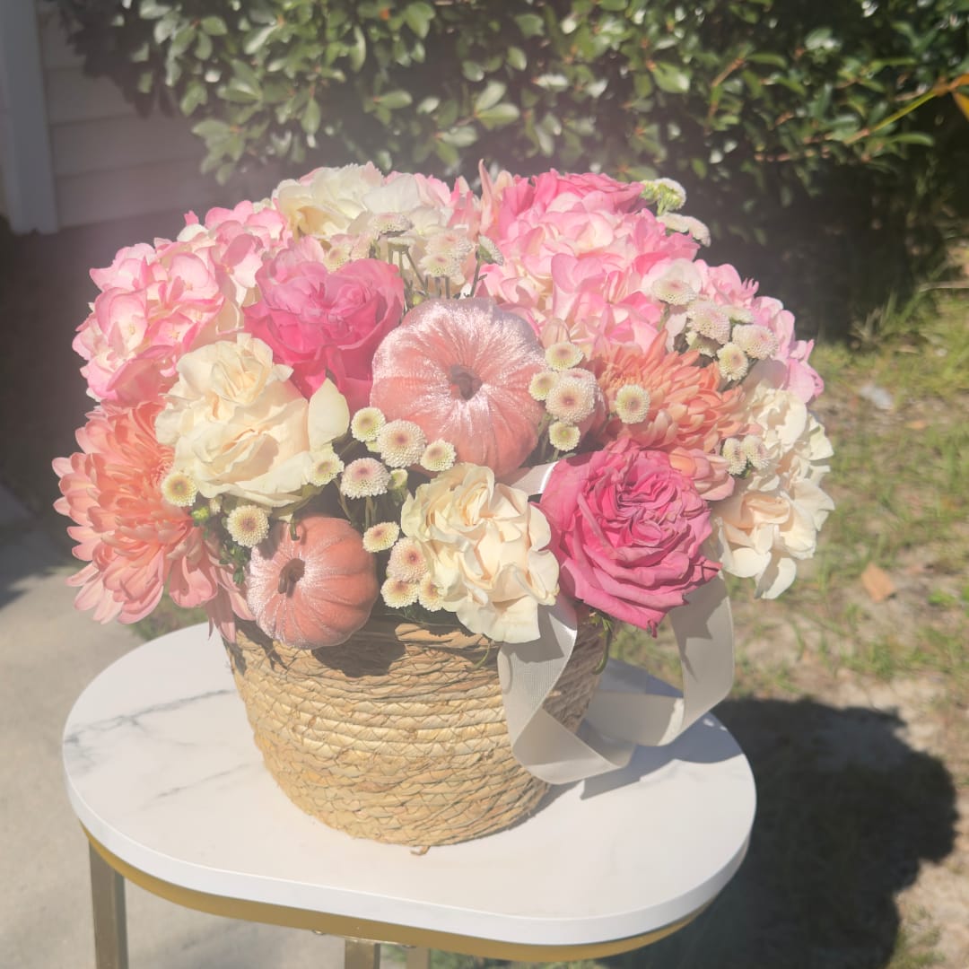 Pink and cream flower arrangement in a woven basket with a ribbon