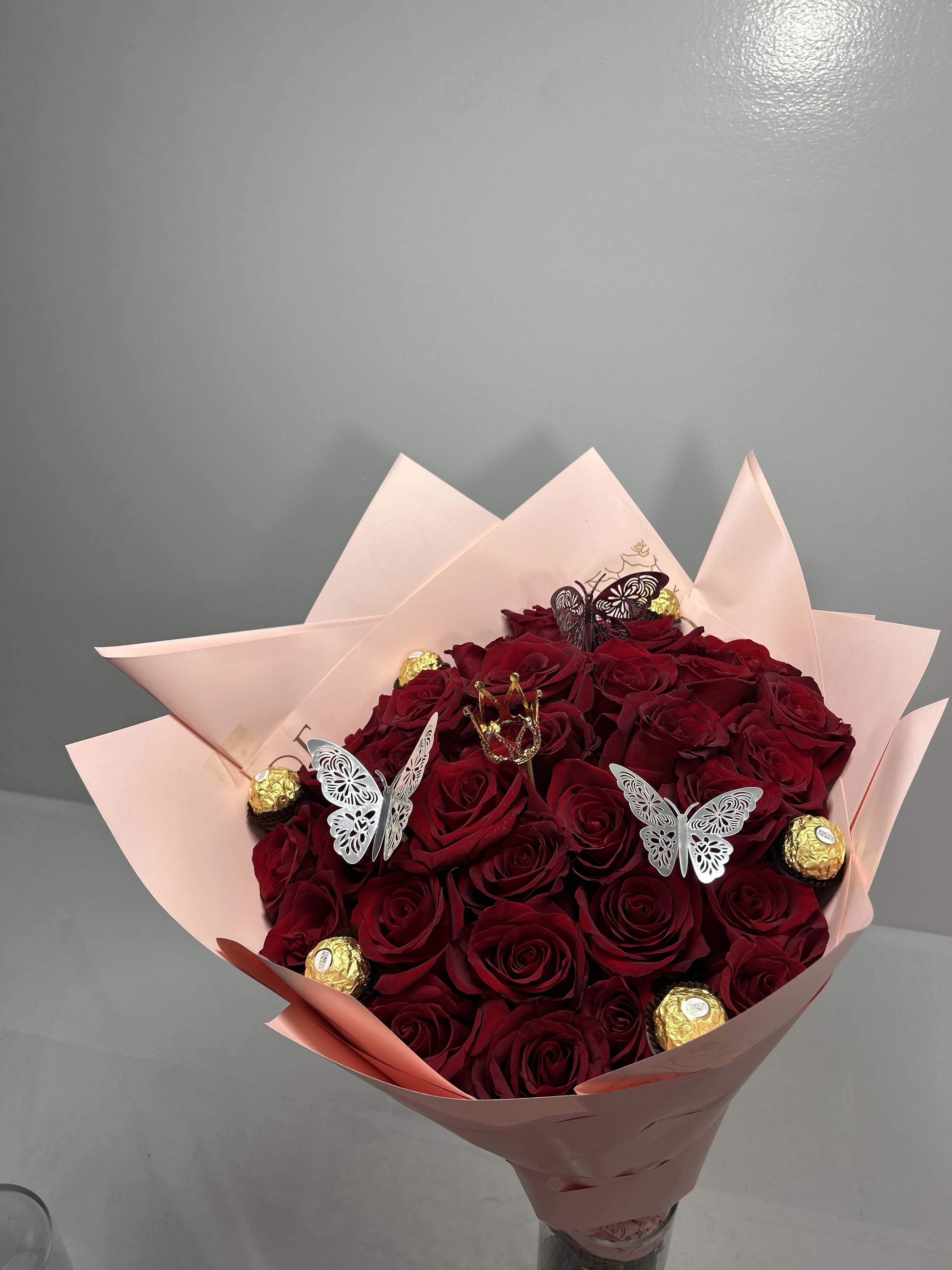 Bouquet of red roses wrapped in pale pink paper with gold chocolates and butterfly picks