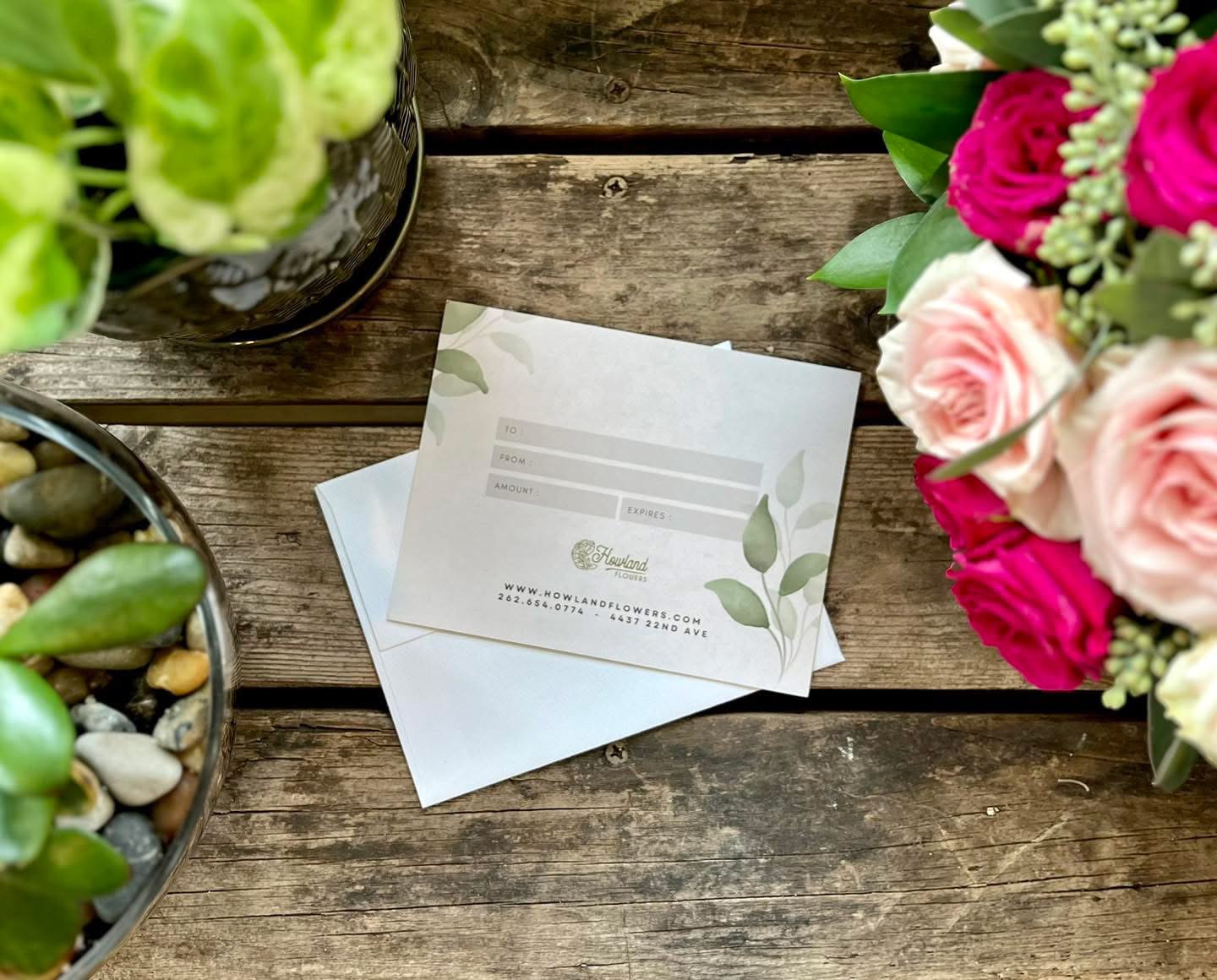 Gift card on a rustic wooden table beside flower arrangements