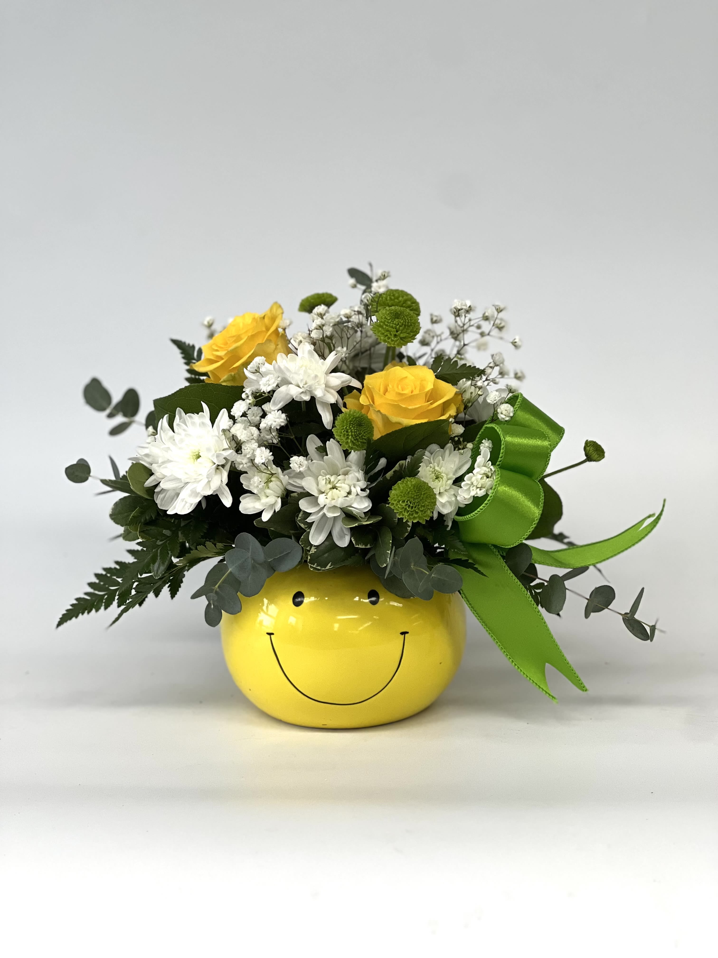 Yellow and white flower arrangement in a smiley-face pot with a green ribbon
