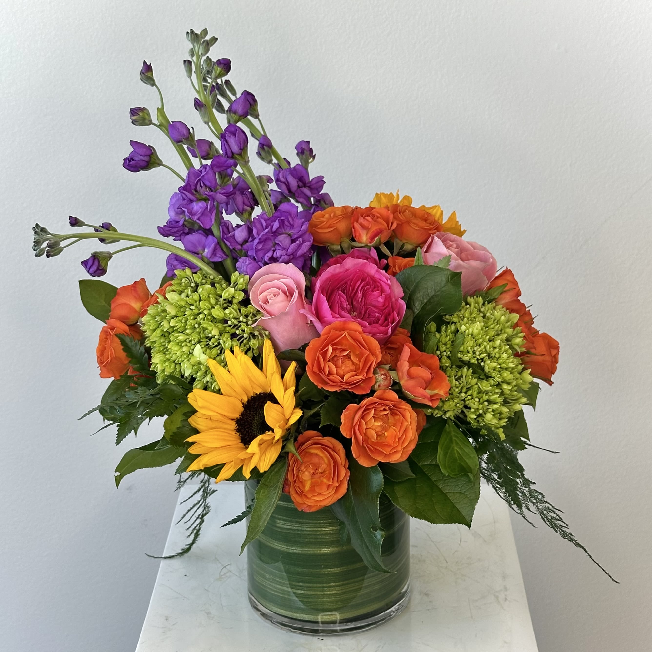 Colorful bouquet with sunflowers, roses, and purple blooms in a glass vase