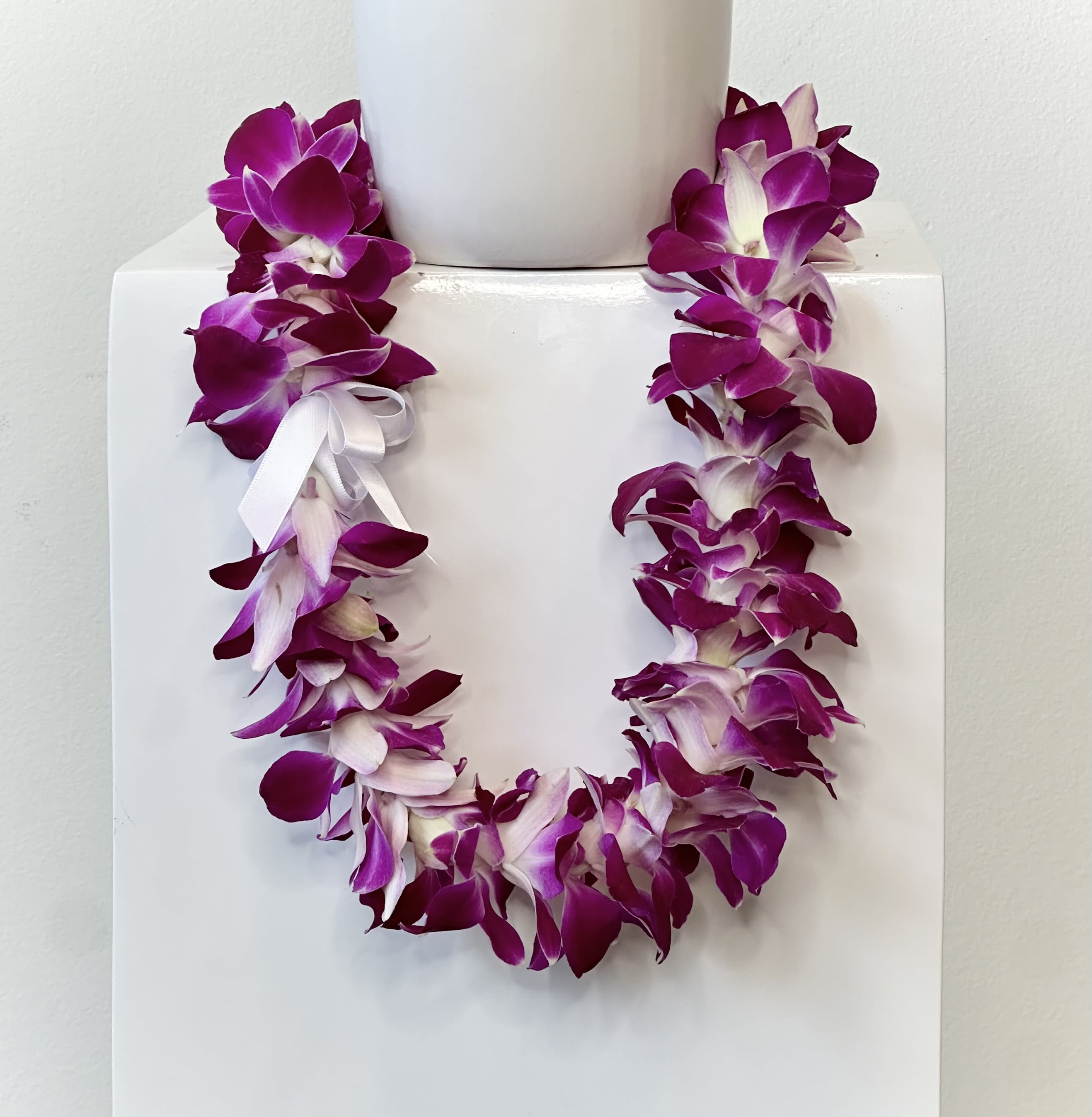 Orchid Lei - Celebrate a meaningful milestone with a beautifully crafted Orchid Lei, a timeless symbol of achievement, honor, and new beginnings. Featuring fresh, vibrant dendrobium orchid blooms, this elegant lei is designed to make any graduate feel celebrated on their special day. Orchids are known for their beauty and longevity, representing love, strength, and success—making them the perfect flower to commemorate such an important accomplishment.  Each lei is handmade in-house using traditional techniques, honoring the cultural significance and artistry behind this cherished Hawaiian tradition. Carefully strung with attention to detail, every orchid lei reflects quality craftsmanship and a thoughtful, personal touch that sets it apart from mass-produced alternatives.  Ideal for graduation ceremonies, photos, and celebrations, this orchid lei adds a bright and festive accent to any outfit while creating lasting memories. Its soft texture and vibrant color make it both comfortable to wear and visually striking.  Whether you are celebrating a high school, college, or advanced degree graduate, this Orchid Lei is a meaningful and elegant way to show pride, love, and support as they step into their next chapter.  Available in purple (featured) or white. Please allow us at least a 2 day heads-up to create your lei.