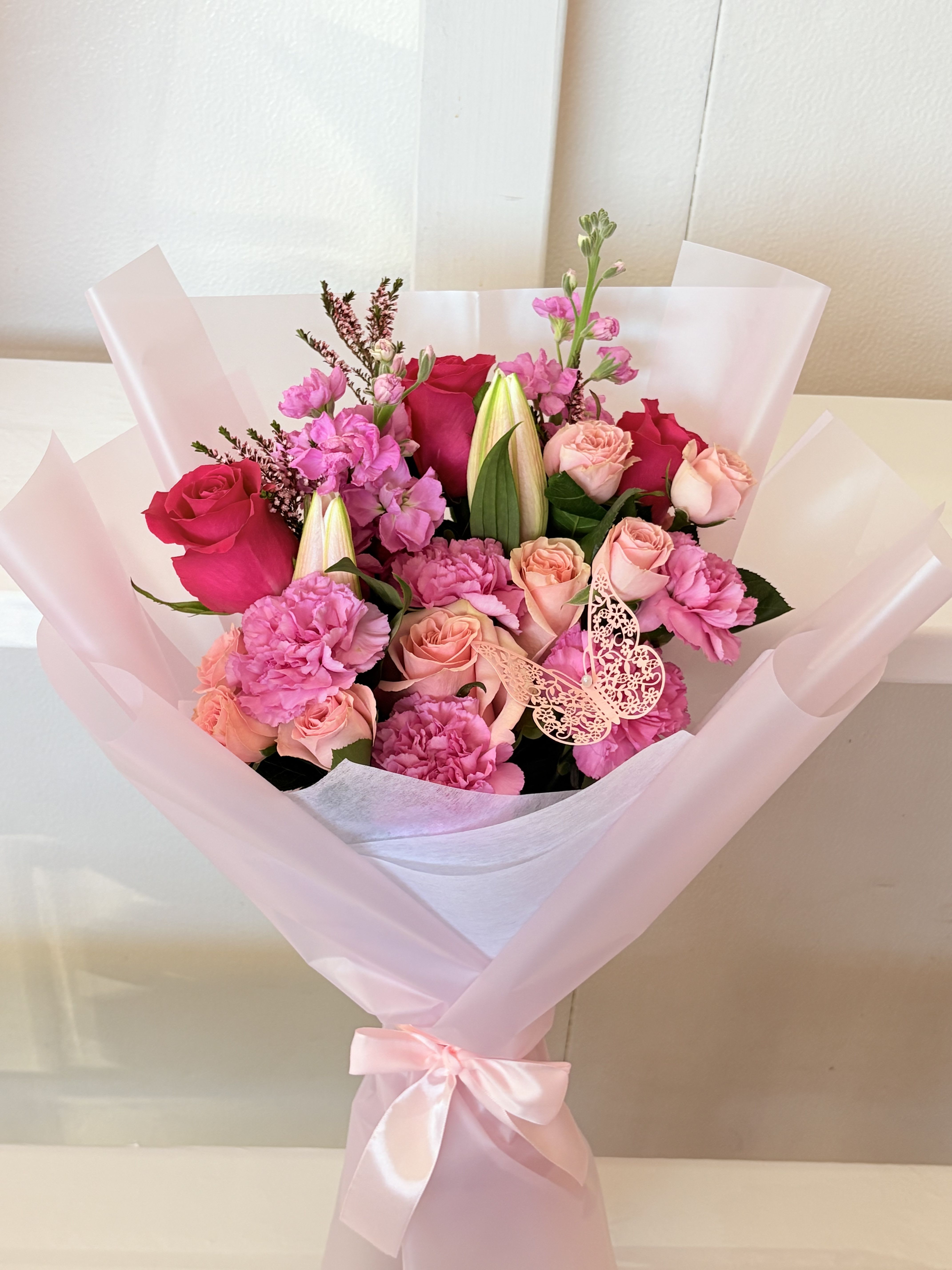 Pink and peach rose bouquet with carnations and lilies in pale pink wrap