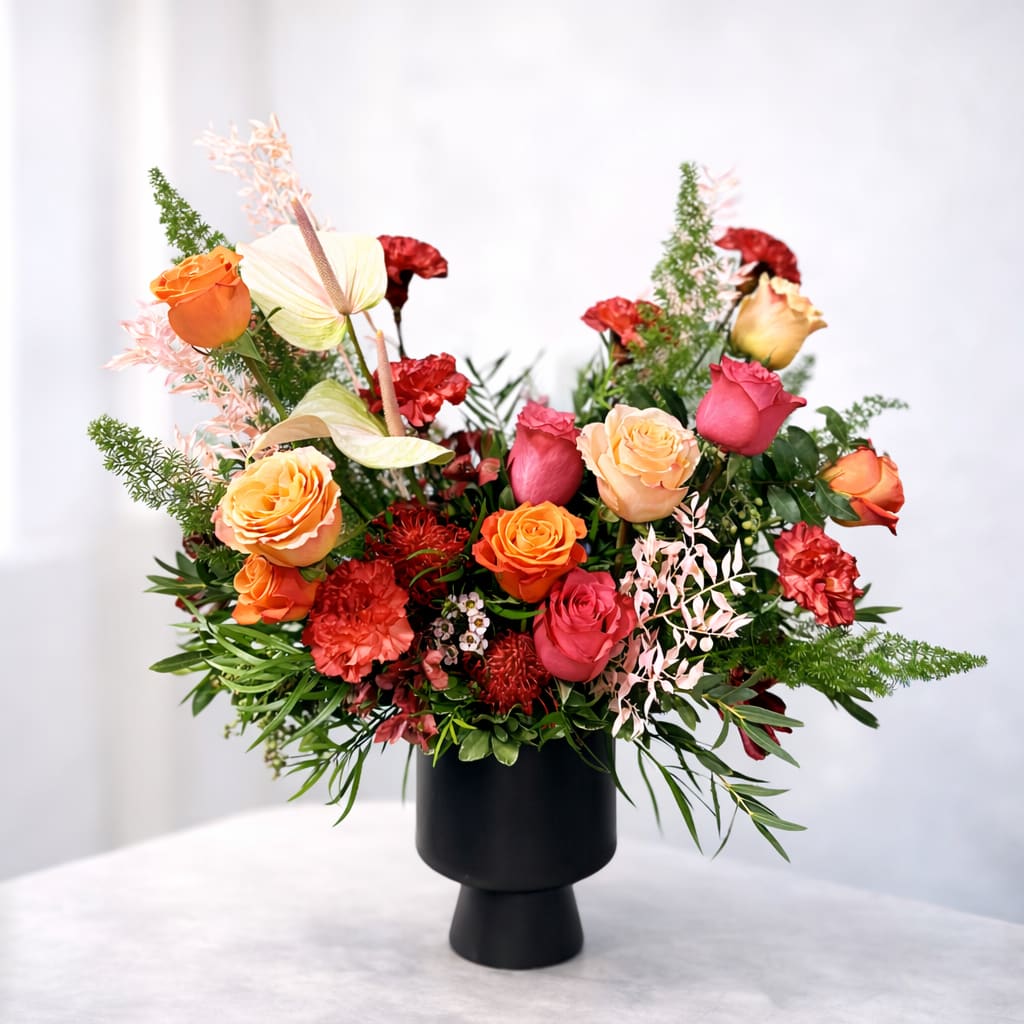 Apollo's Passion - This fiery subtropical arraignment will make a bold statement with vibrant colors and unique textures. Designed in a modern black ceramic container including striking South African pincushion protea, hot-pink Ecuadorian roses, and dried Italian ruscus. This is the perfect way to express your passion with your current flame or celebrate an exciting advancement.