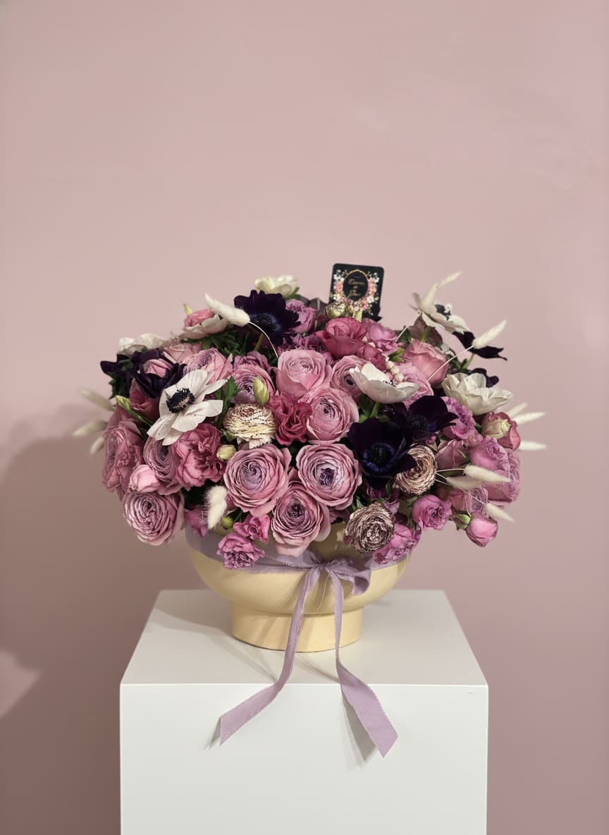 Pink and purple bouquet in a round box with a lavender ribbon